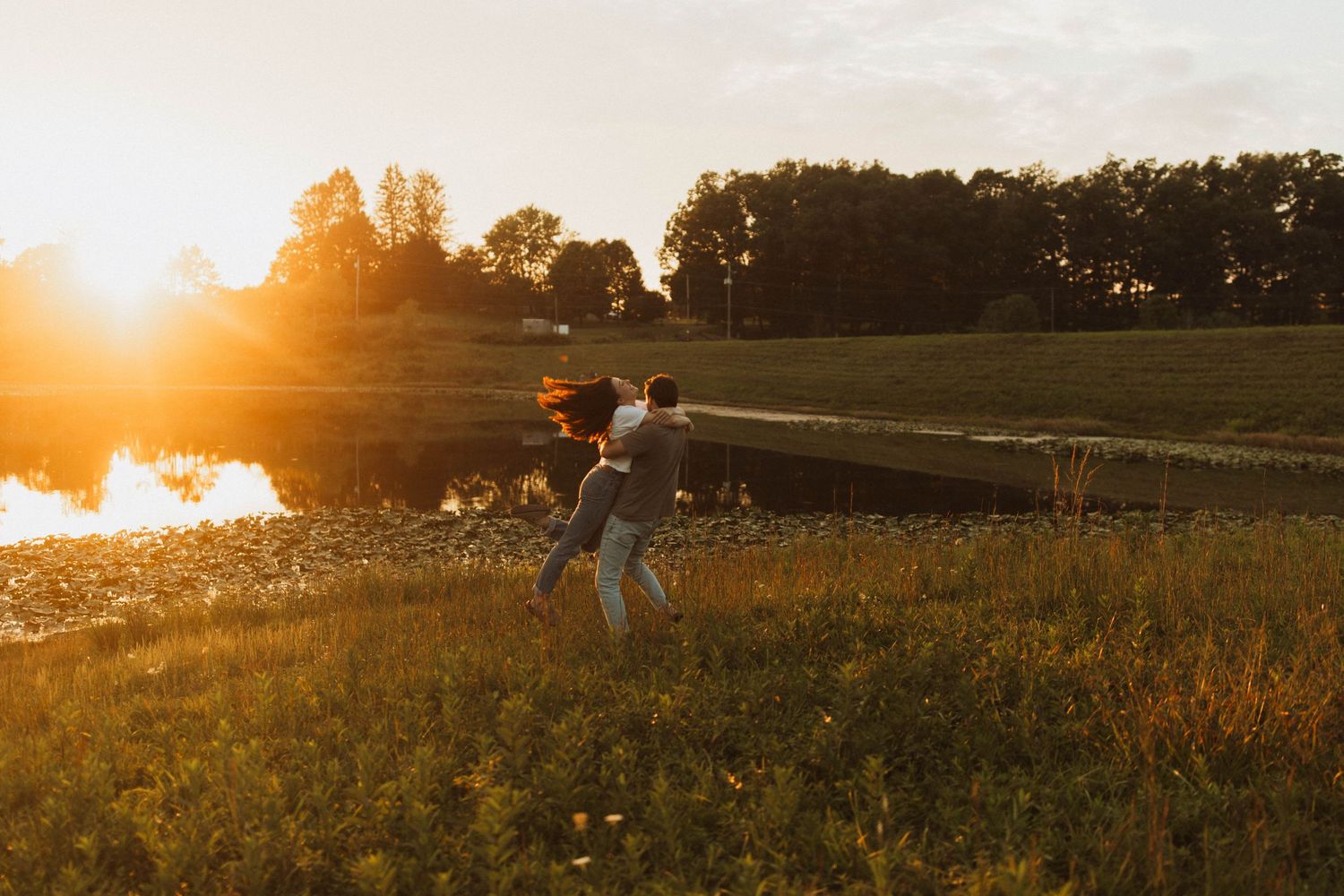 Person jumping joyfully in a field during sunset near a lake.