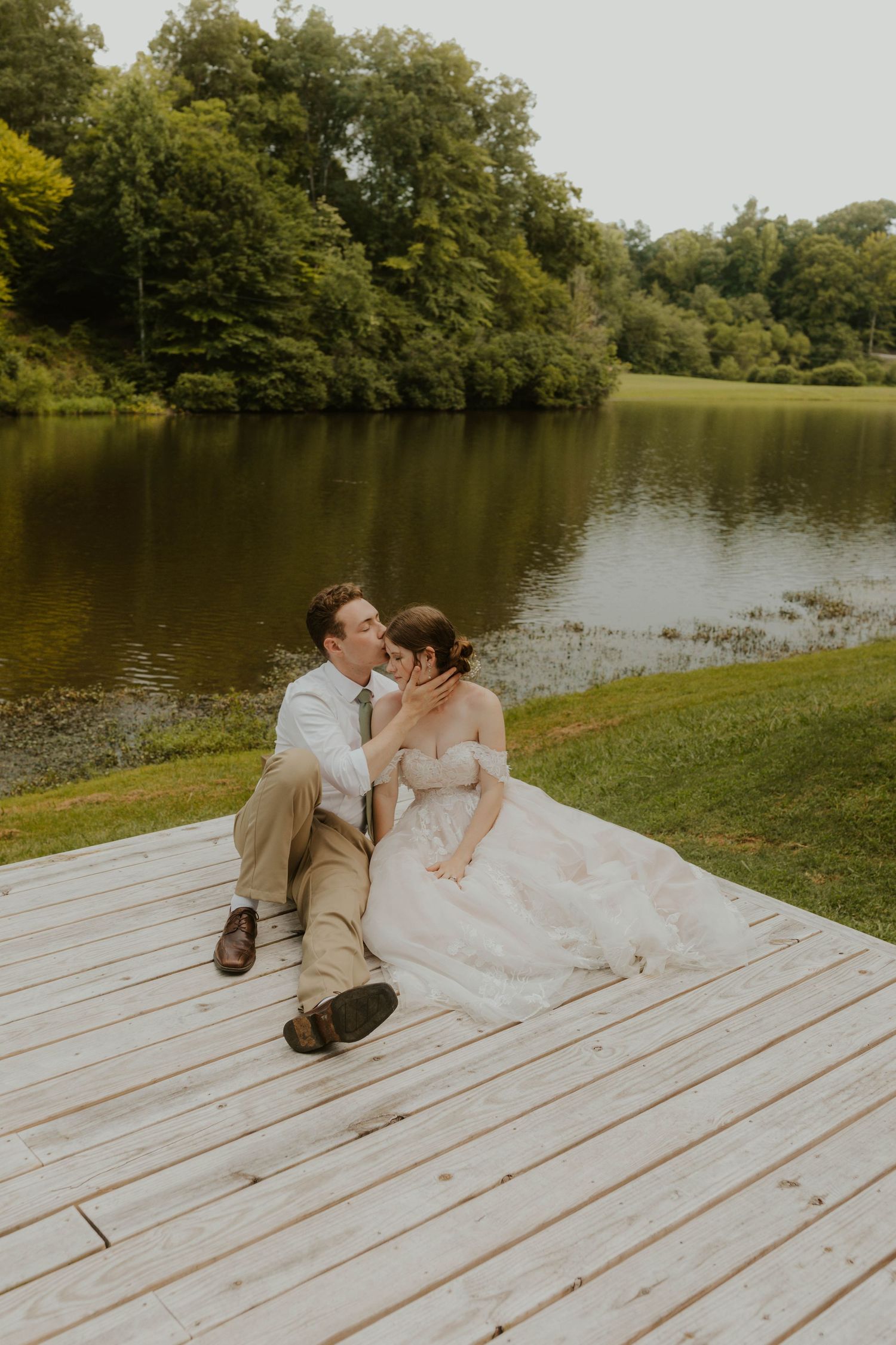 Wedding couple relaxing on wooden dock by serene lake.