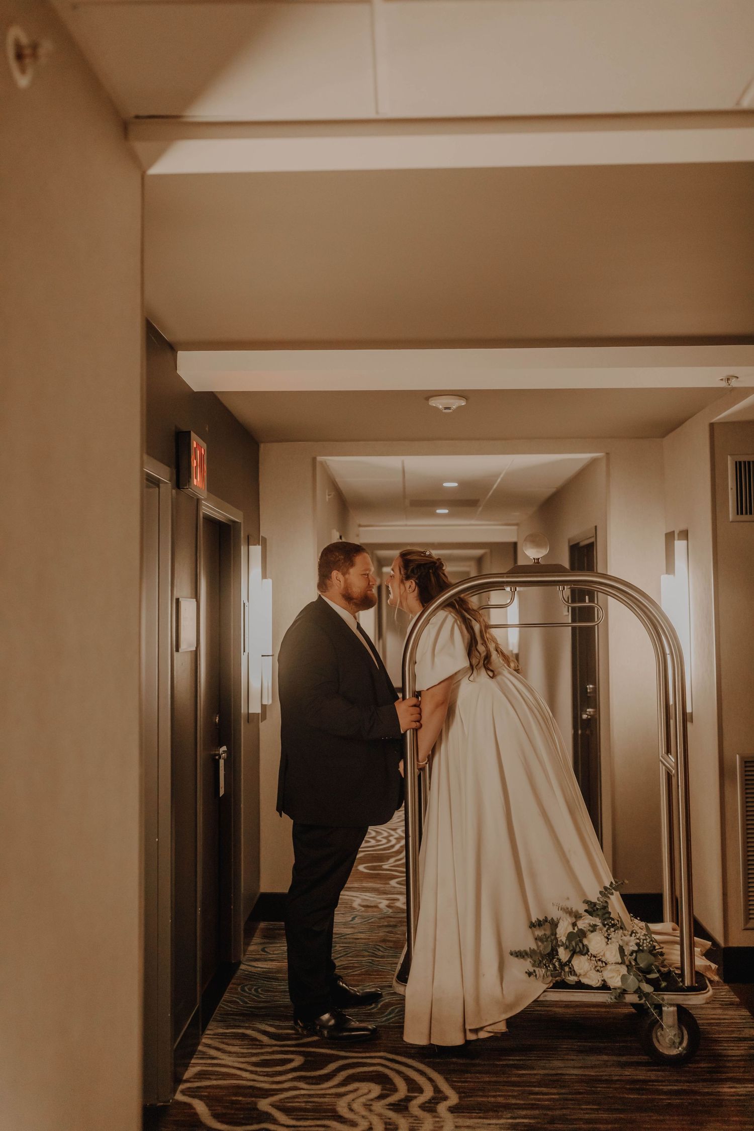 A tender moment shared in a hotel hallway with luggage cart and warm lighting.