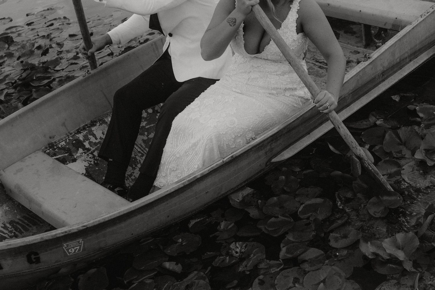Black and white photo of a couple sitting in a rowboat surrounded by lily pads.