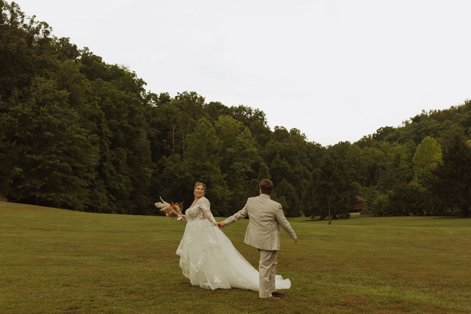 Couple running together across an open grassy field during their wedding day.
