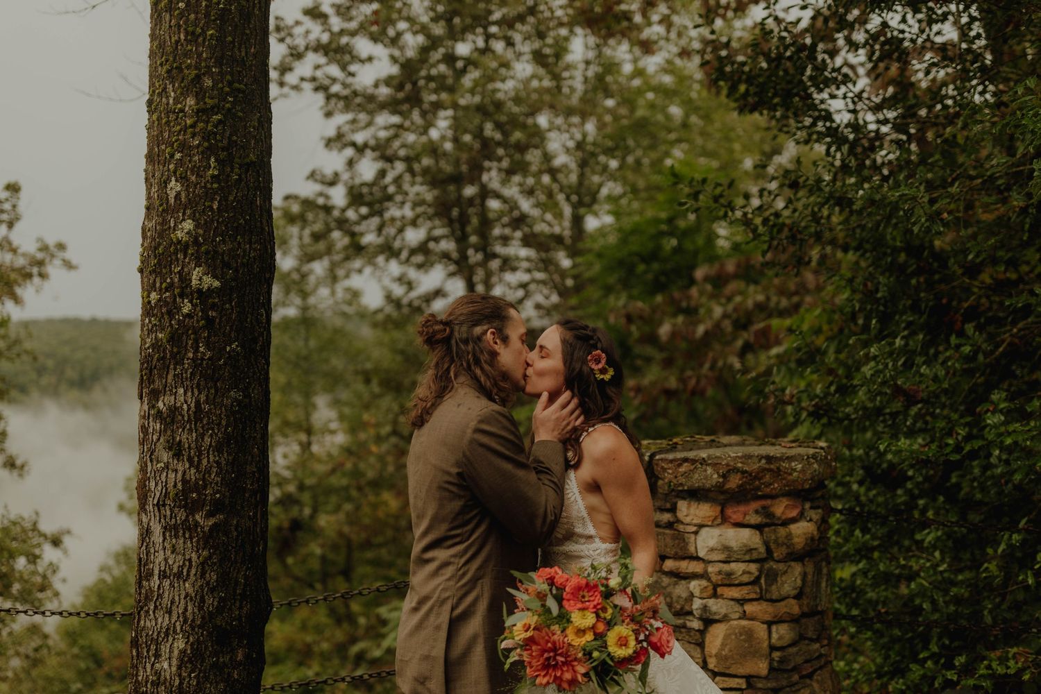 Intimate wedding moment captured between stone pillars with fall foliage in background.