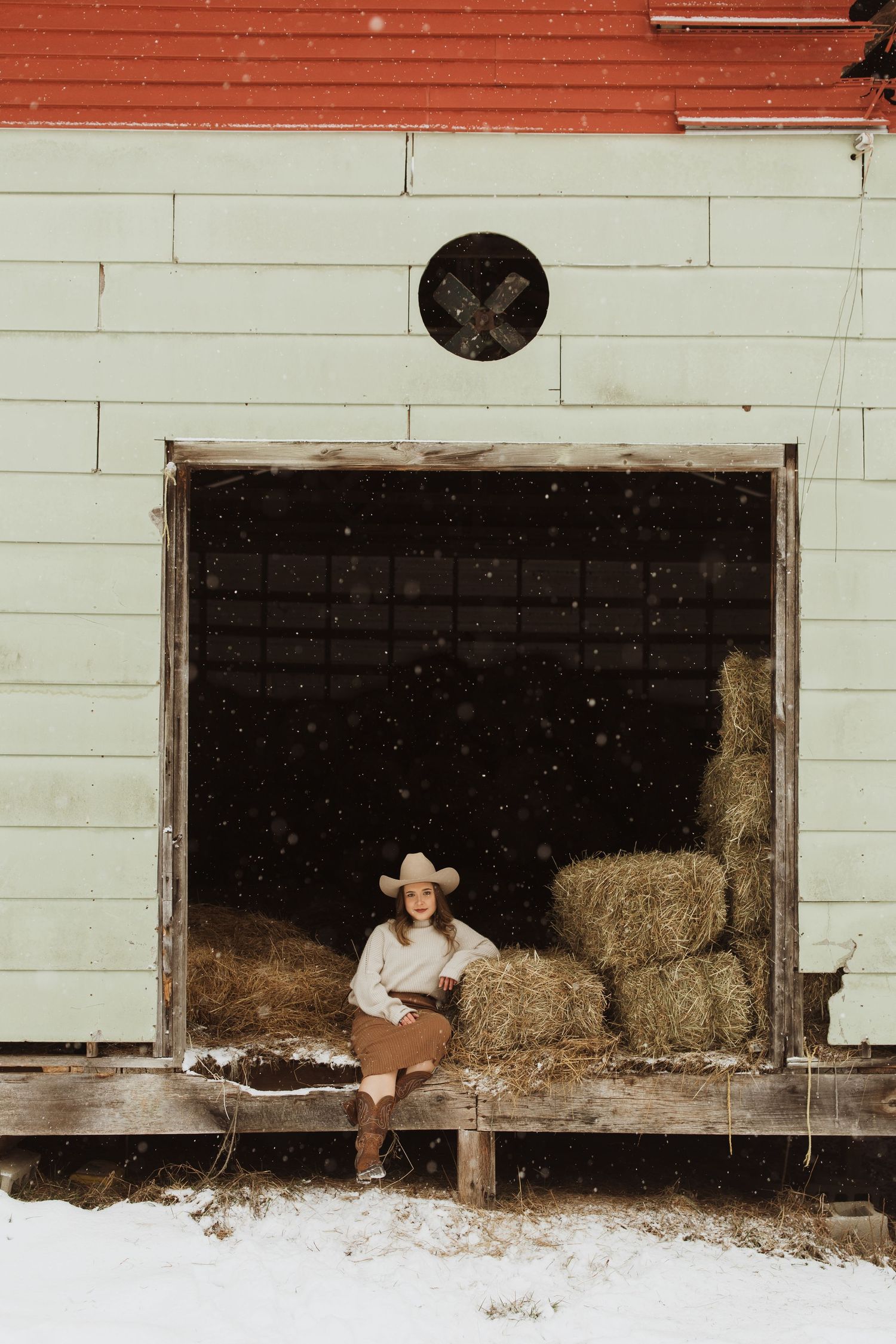 A rustic winter portrait in a barn doorway with hay bales.