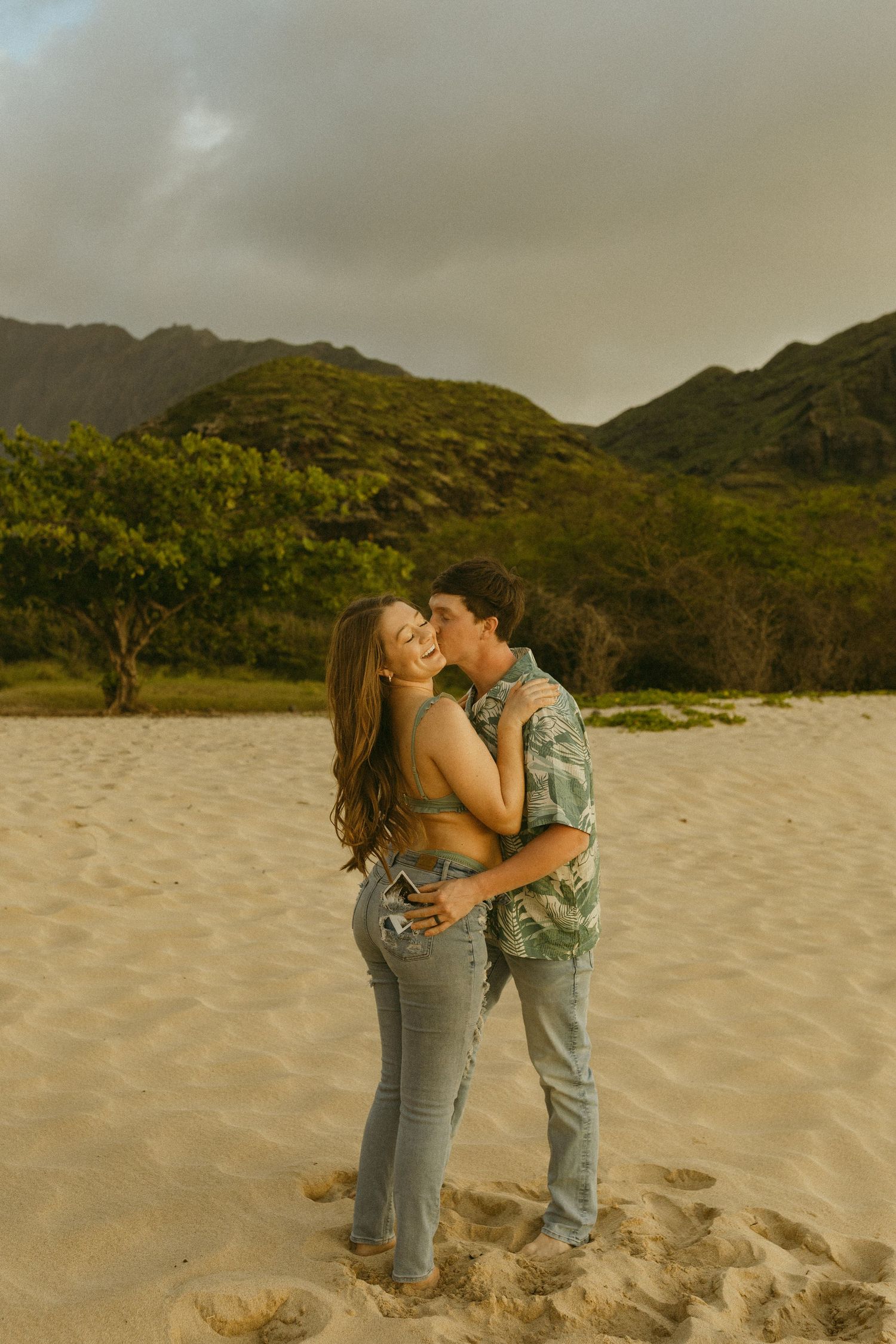 Intimate moment captured between couple on beach with mountains in background.