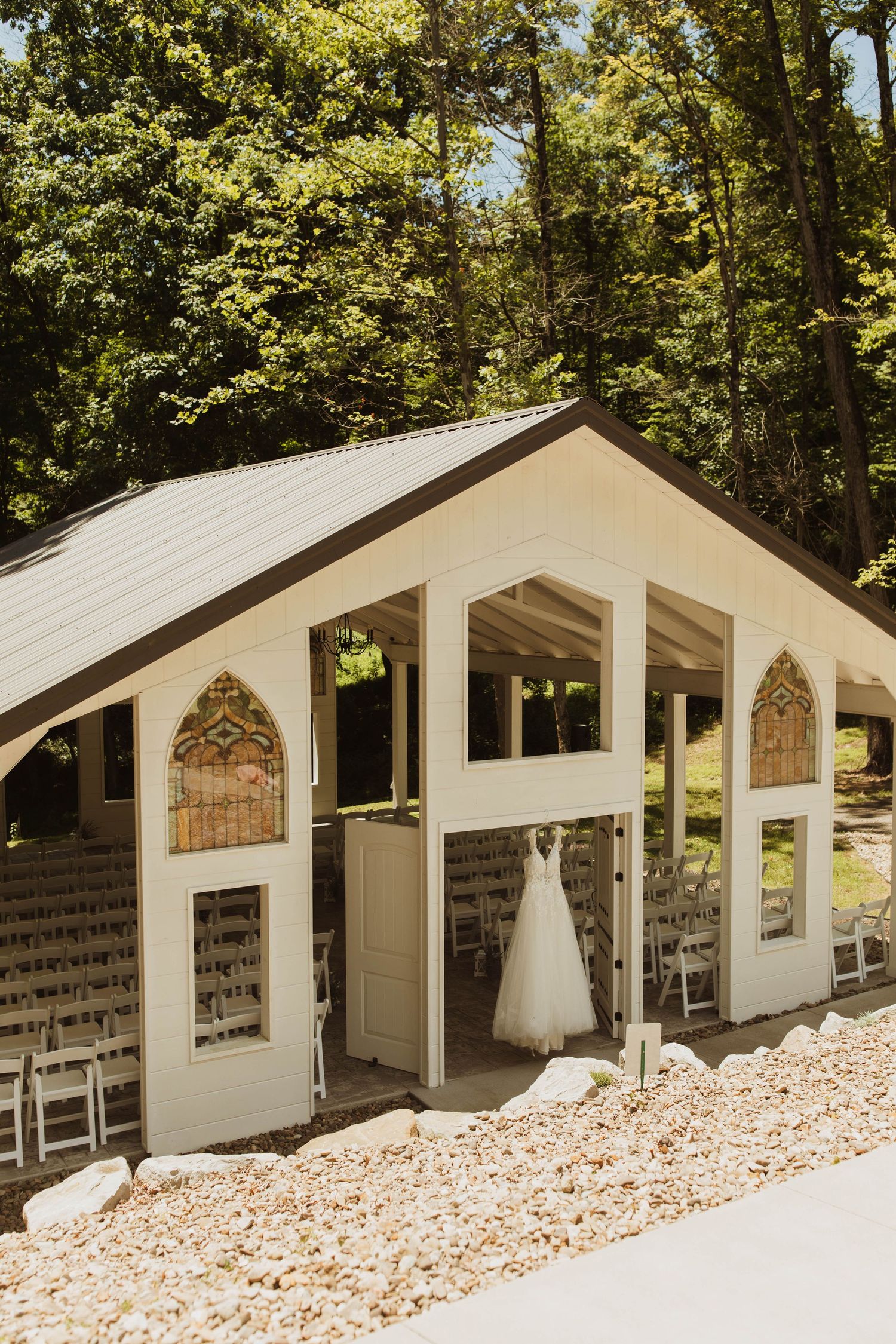 White chapel wedding venue nestled in the woods with a wedding dress displayed in the window.