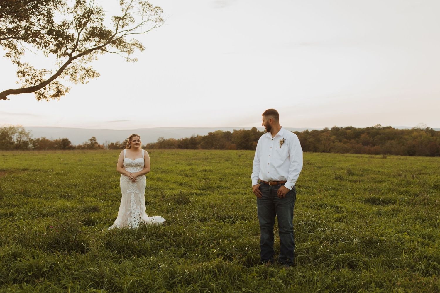 A couple shares a playful moment in a grassy field during their wedding photoshoot.
