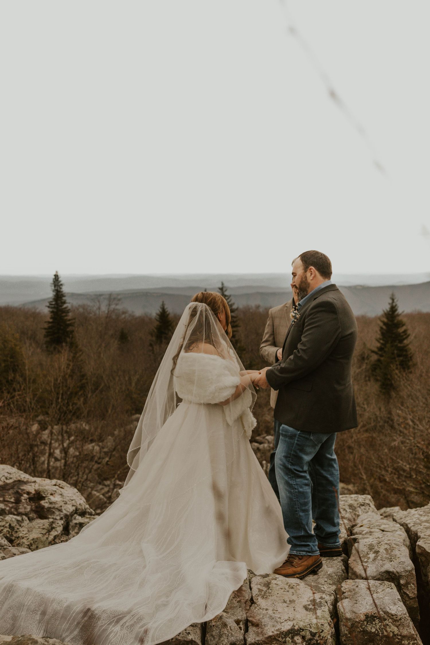Wedding couple standing on rocky overlook with dramatic landscape view.