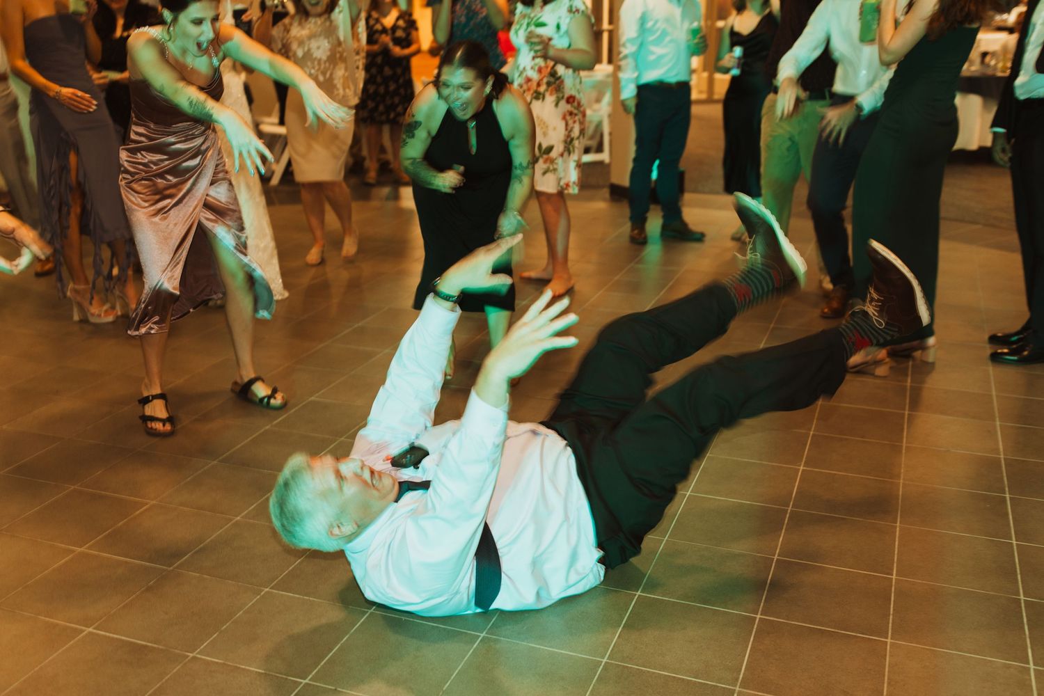 Wedding guest performs energetic dance move on reception floor with green lighting.