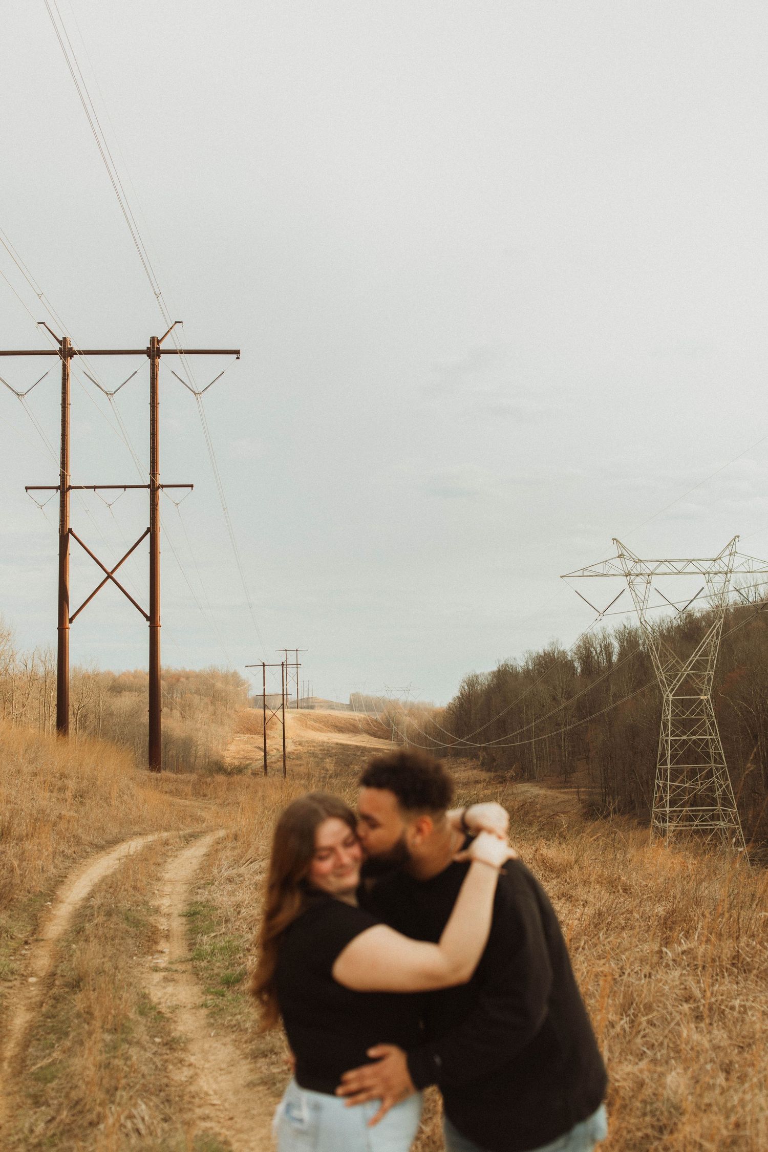 Romantic embrace on dirt path with power lines in golden field.