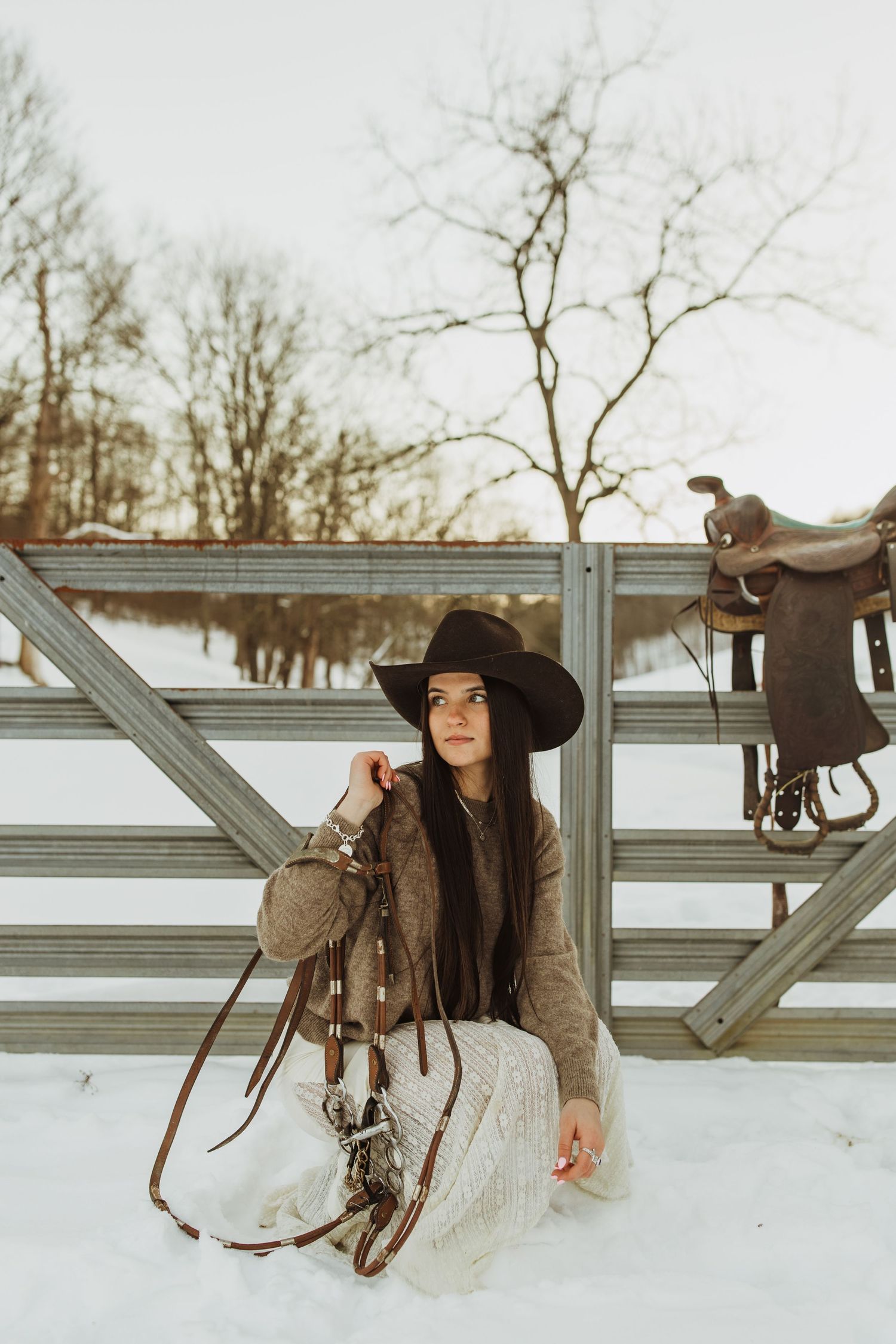 A western-styled photoshoot in snow with horse saddle and rustic fence.