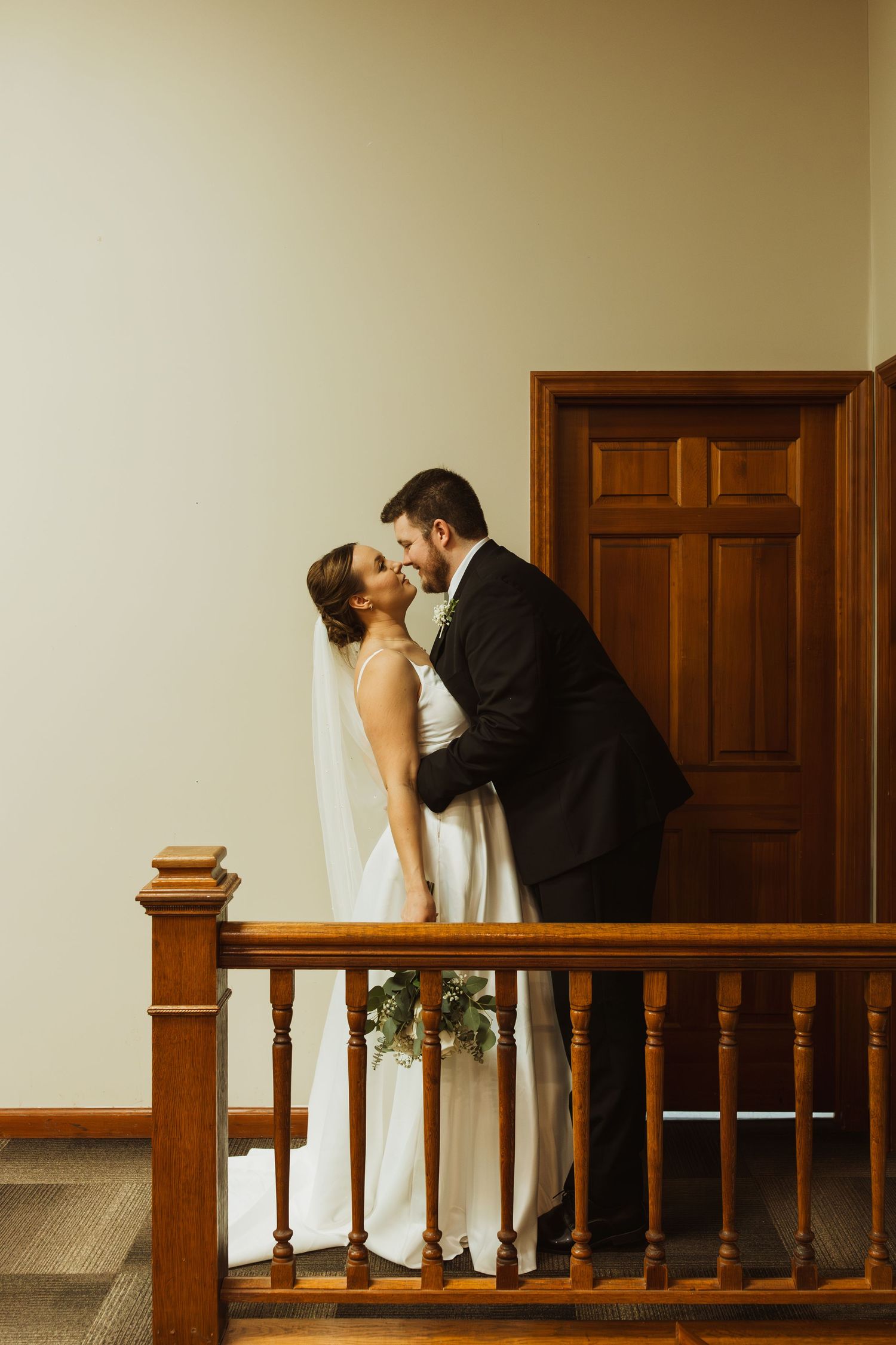 A romantic moment captured between newlyweds on a wooden staircase with a traditional wooden door in the background.