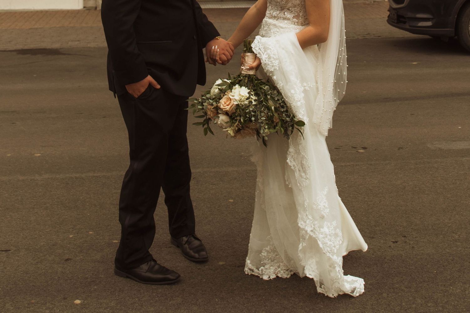Close-up shot of wedding couple's lower half showing bride's lace dress and groom's black suit.