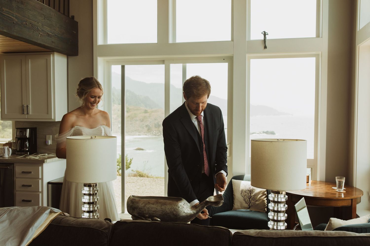 A couple prepares in a modern coastal home with large windows overlooking the ocean.