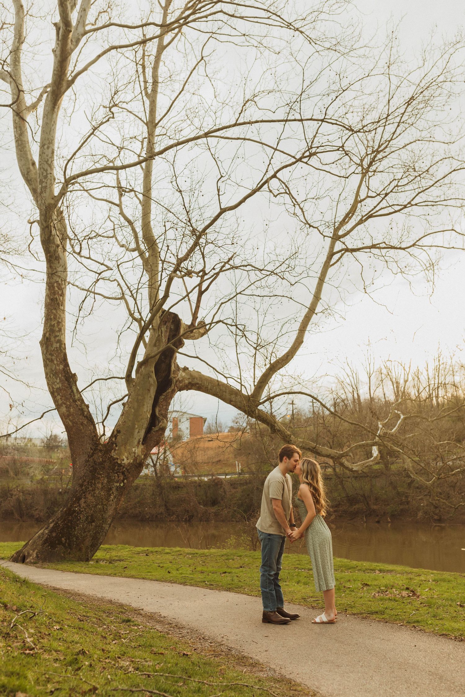 Couple shares intimate moment on path beneath bare winter trees.
