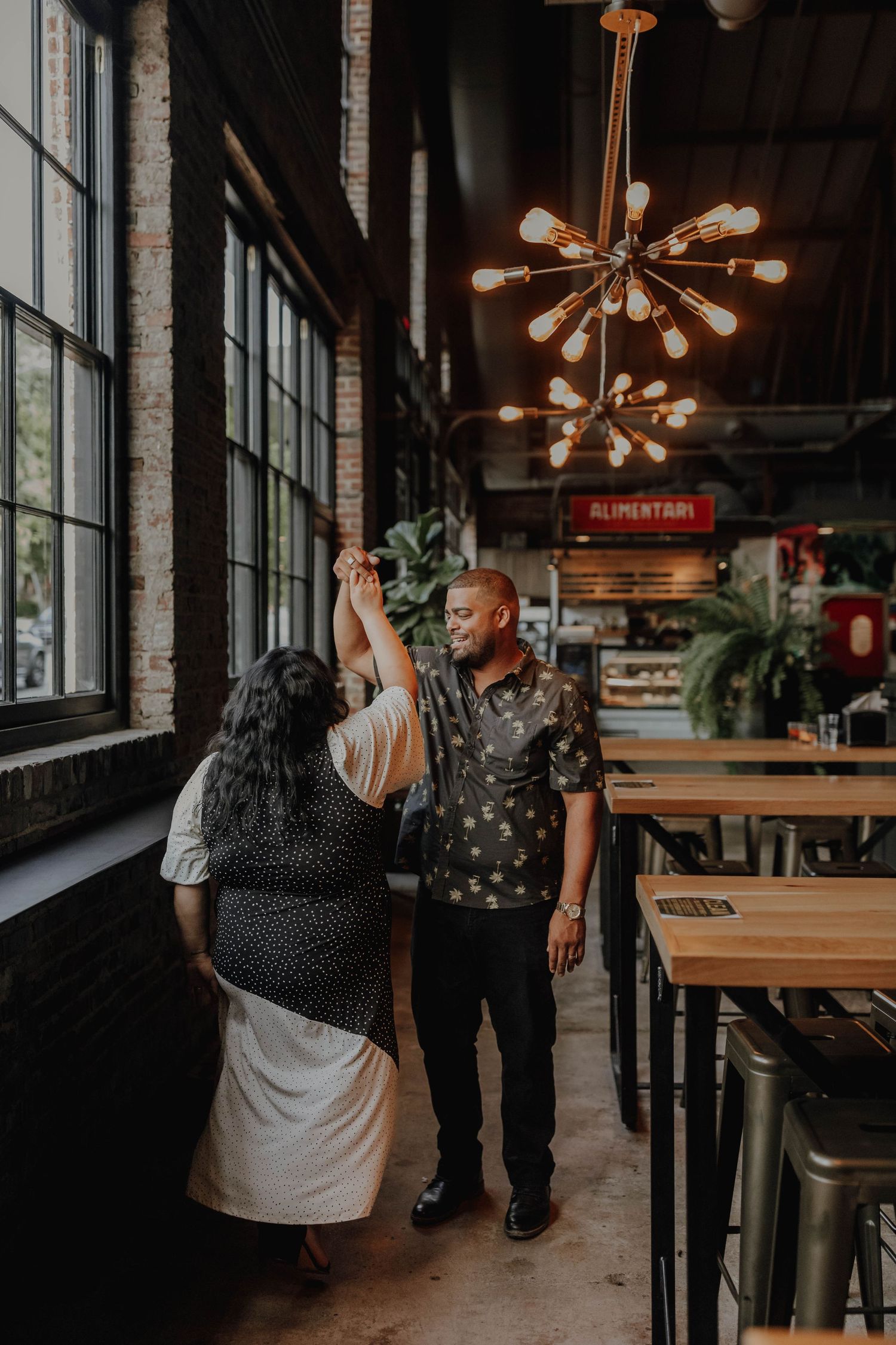 Couple dancing together in an industrial-style restaurant with modern lighting.