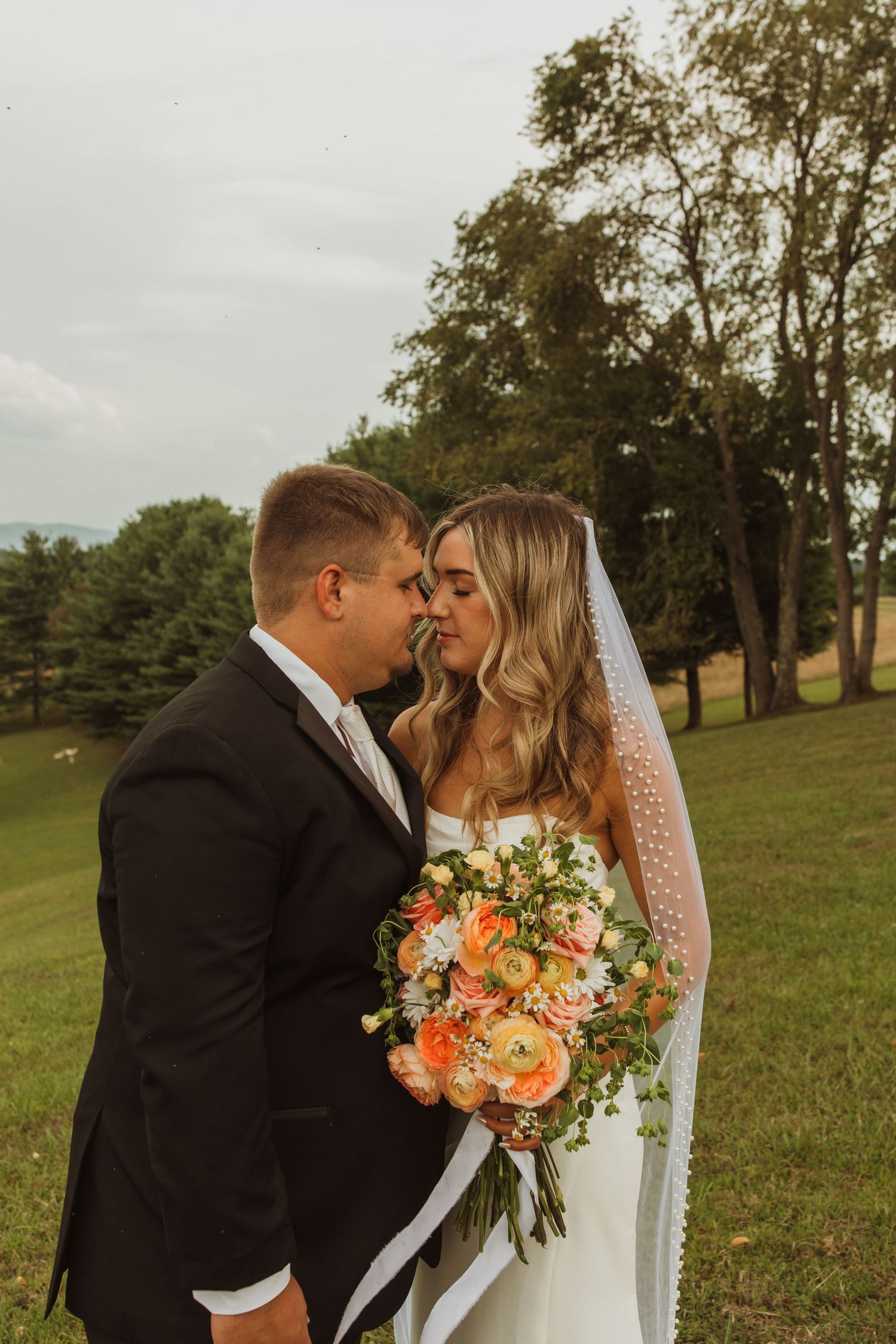 A romantic wedding portrait with a couple and a vibrant orange and peach bouquet.
