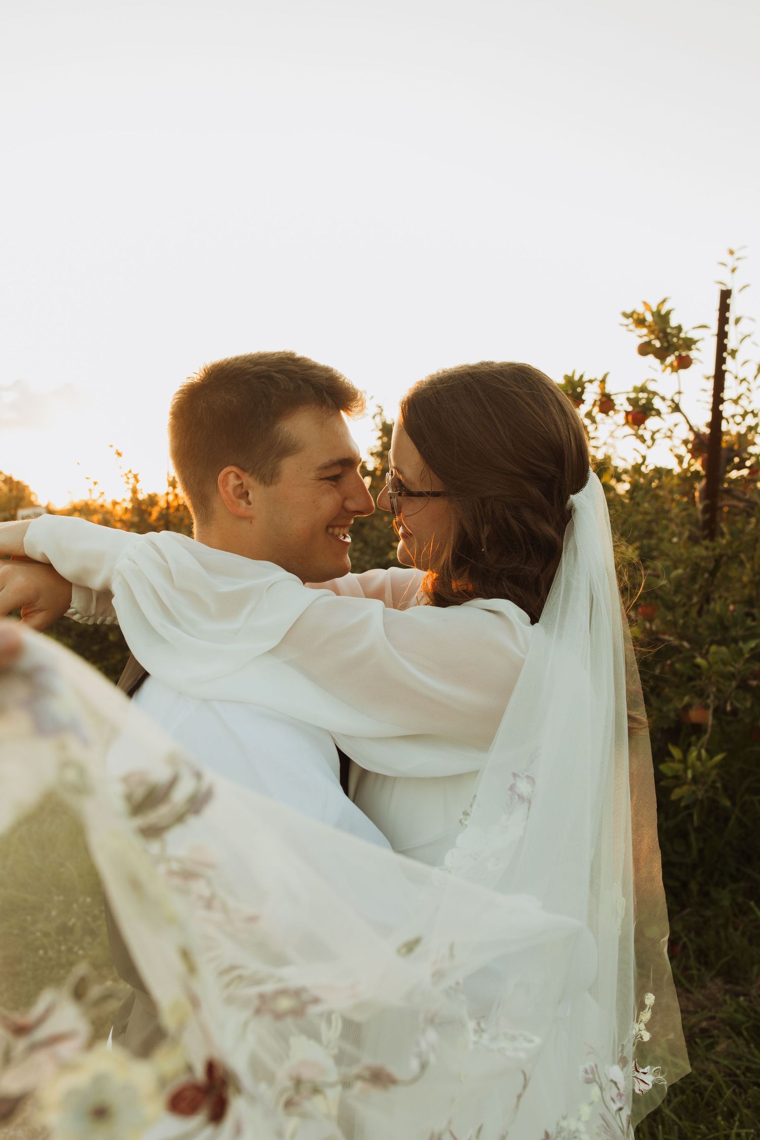 Romantic sunset portrait of newlyweds embracing with flowing veil in golden light.