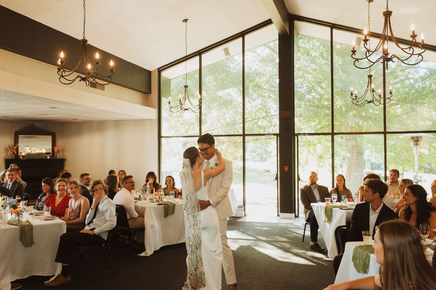 Wedding reception venue with floor to ceiling windows and chandelier during first dance.