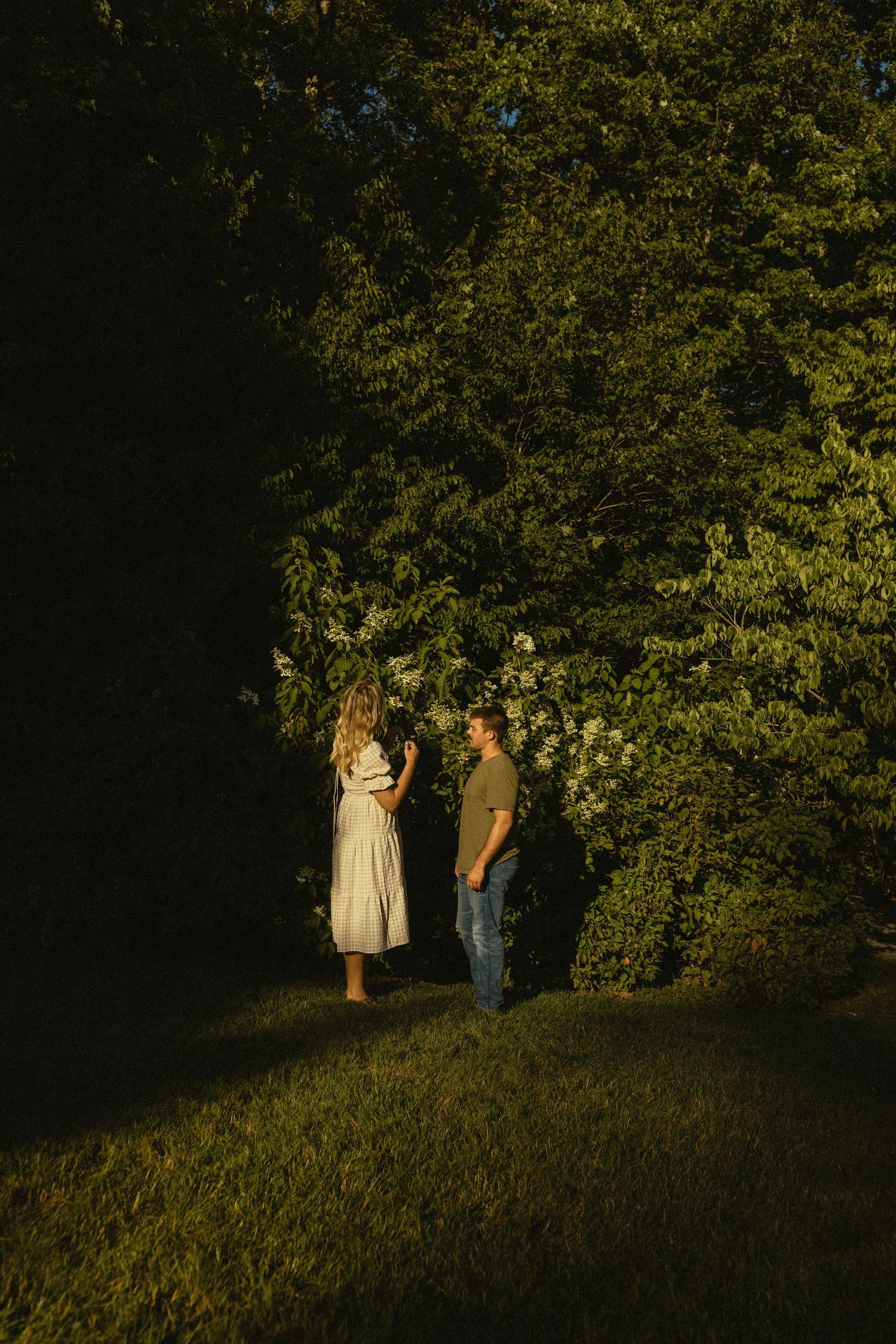 Couple standing in sunlit forest clearing during golden hour.
