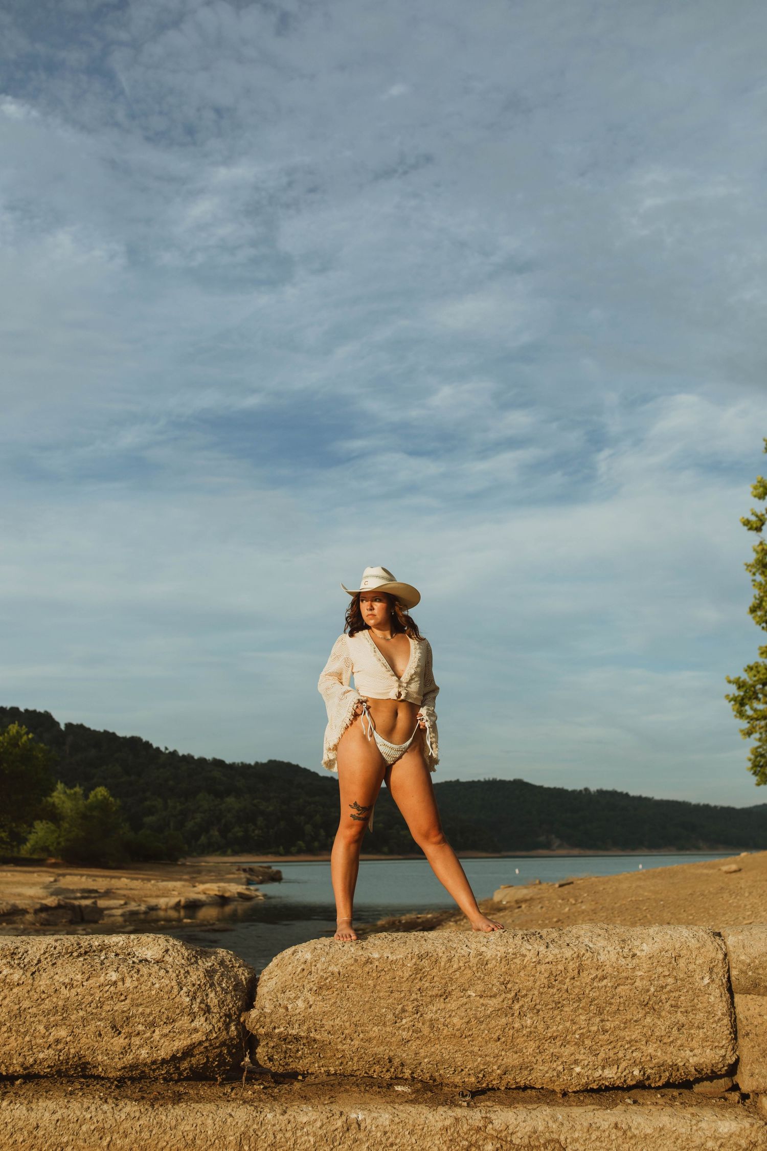 A silhouette strikes a dynamic pose against a bright sky on rocky lakeside terrain.