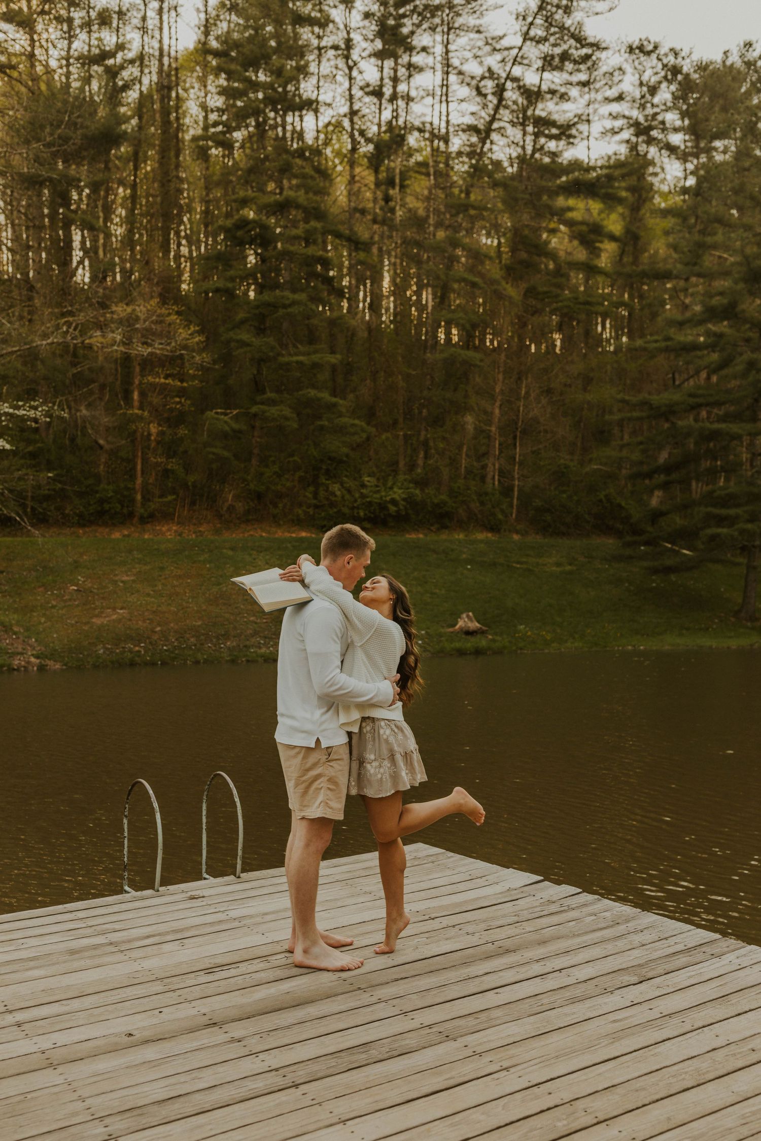 Couple sharing romantic moment on wooden dock by lake at golden hour.
