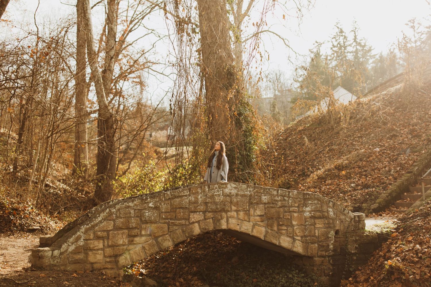 Figure standing on a rustic stone bridge in an autumn forest setting.