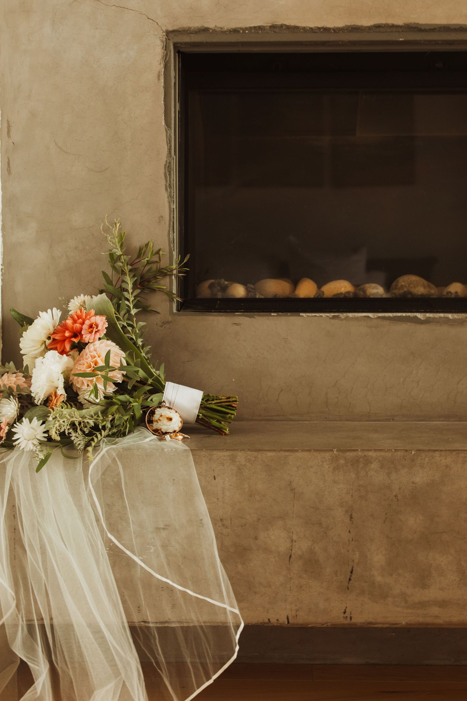 Bridal bouquet with coral and white flowers rests near a modern fireplace.