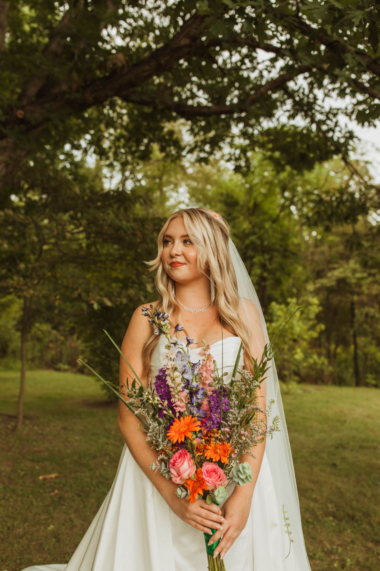 Bride holding vibrant summer wildflower bouquet in a sunlit garden setting.