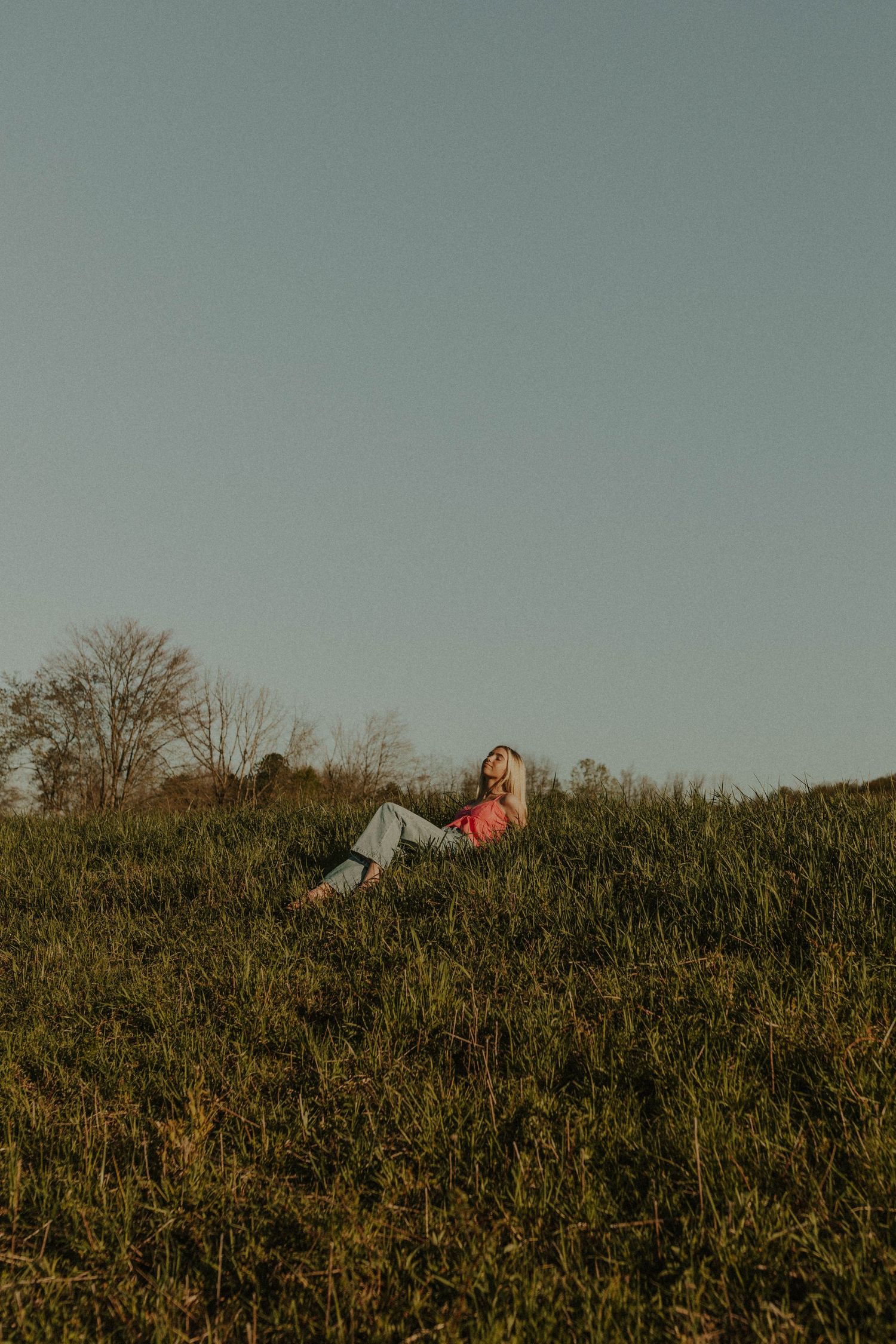 Someone lounging in a grassy field at sunset wearing an orange top.