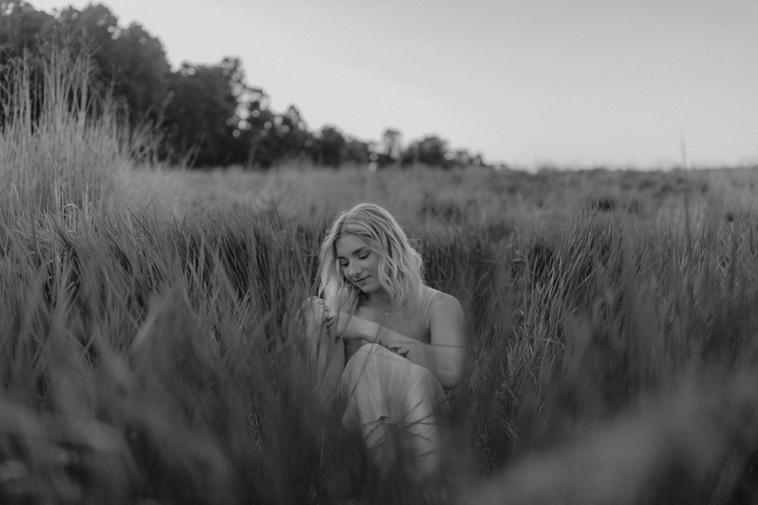 Black and white portrait of person kneeling in tall grass field.