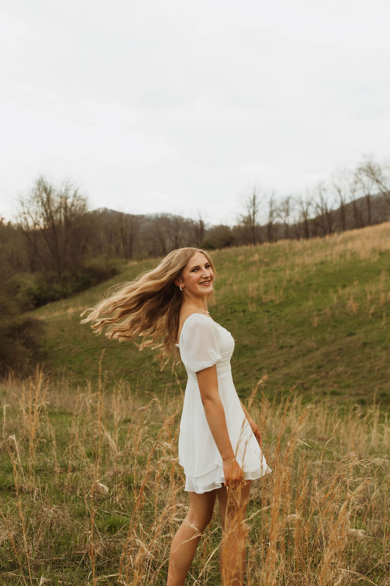 A white dress flows in the wind as someone twirls on a grassy hillside.