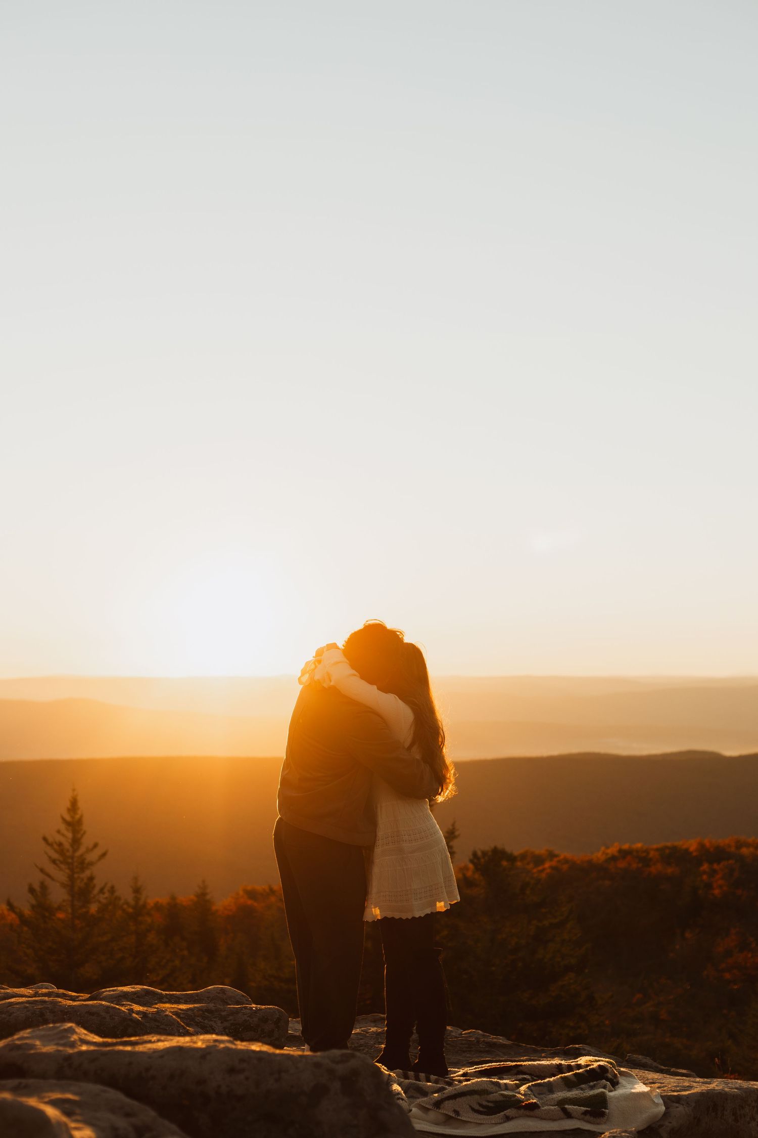 Two silhouettes embracing on a mountain peak during golden hour sunset.