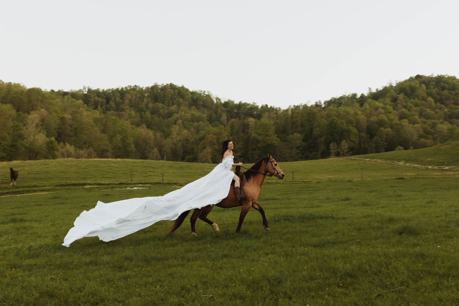 A flowing white wedding dress trails behind as someone rides horseback across a green meadow.