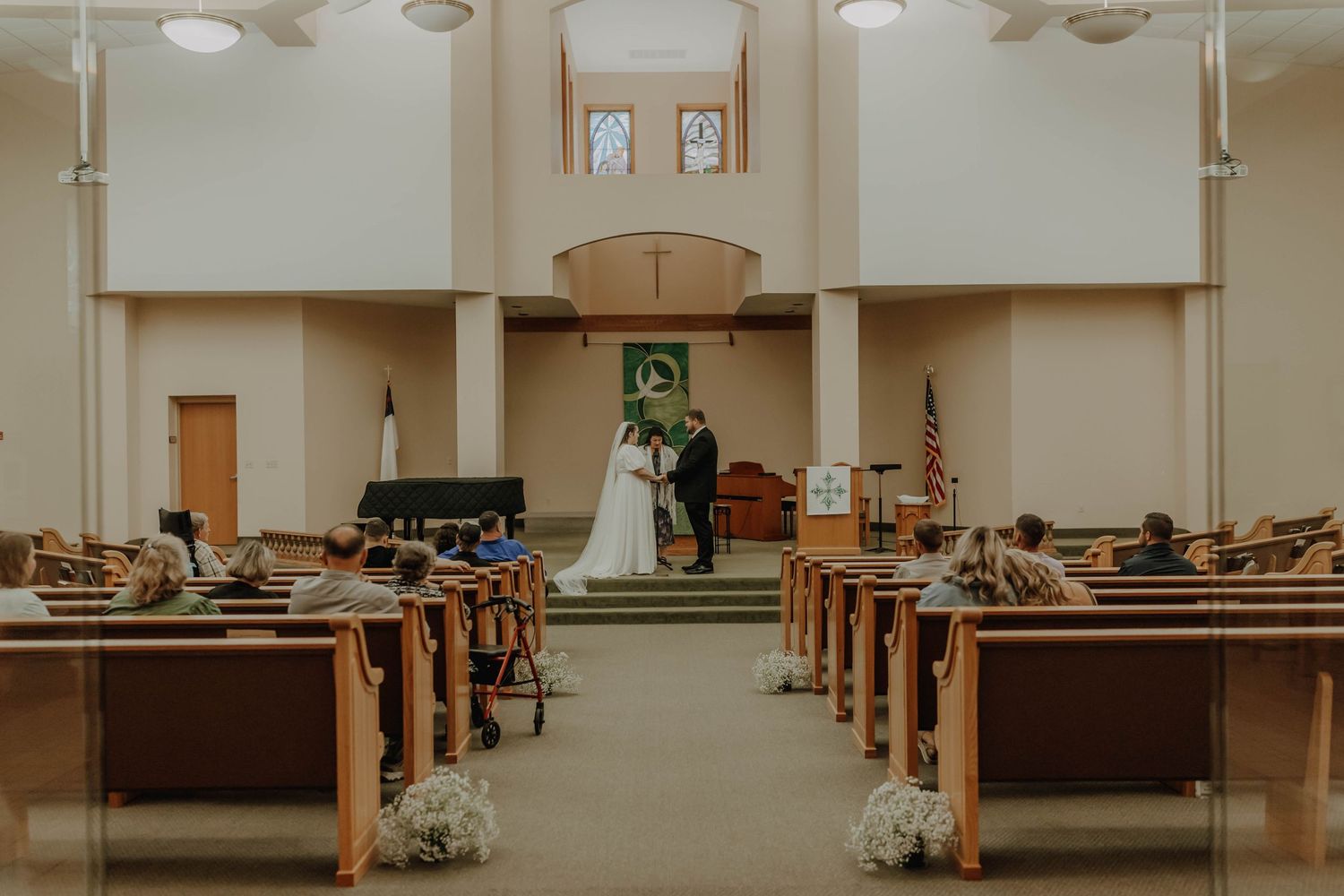 Interior of a church with wooden pews and floral decorations during a wedding ceremony.
