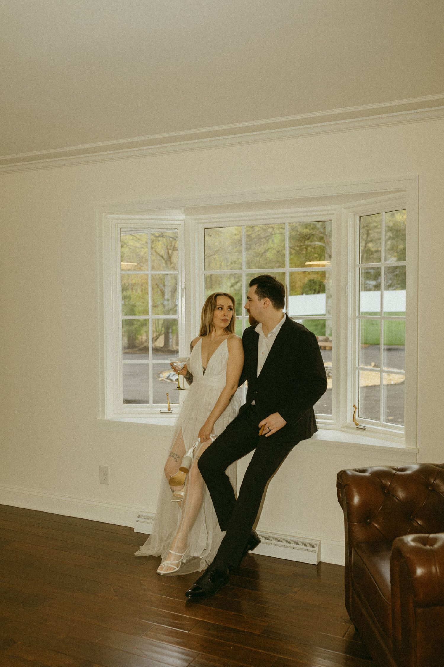 Couple in formal attire share a romantic moment by a bright window in an elegant room.