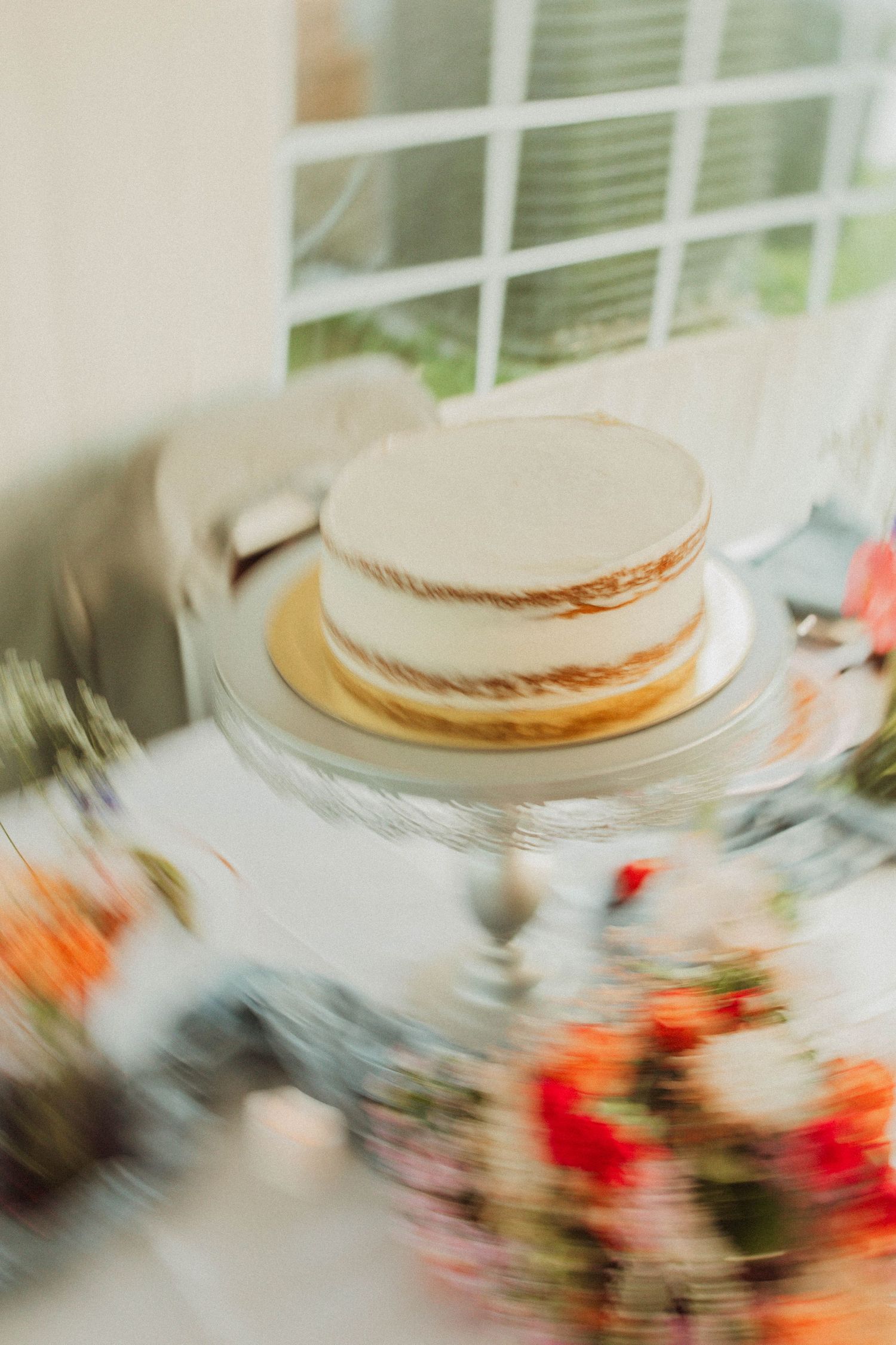 Simple white wedding cake on display with blurred floral decorations in foreground.