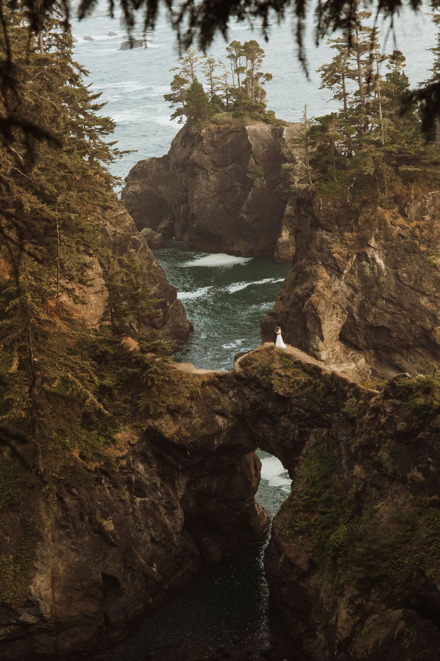 Dramatic coastal rock formation with natural bridge arch and crashing waves along a rugged shoreline.
