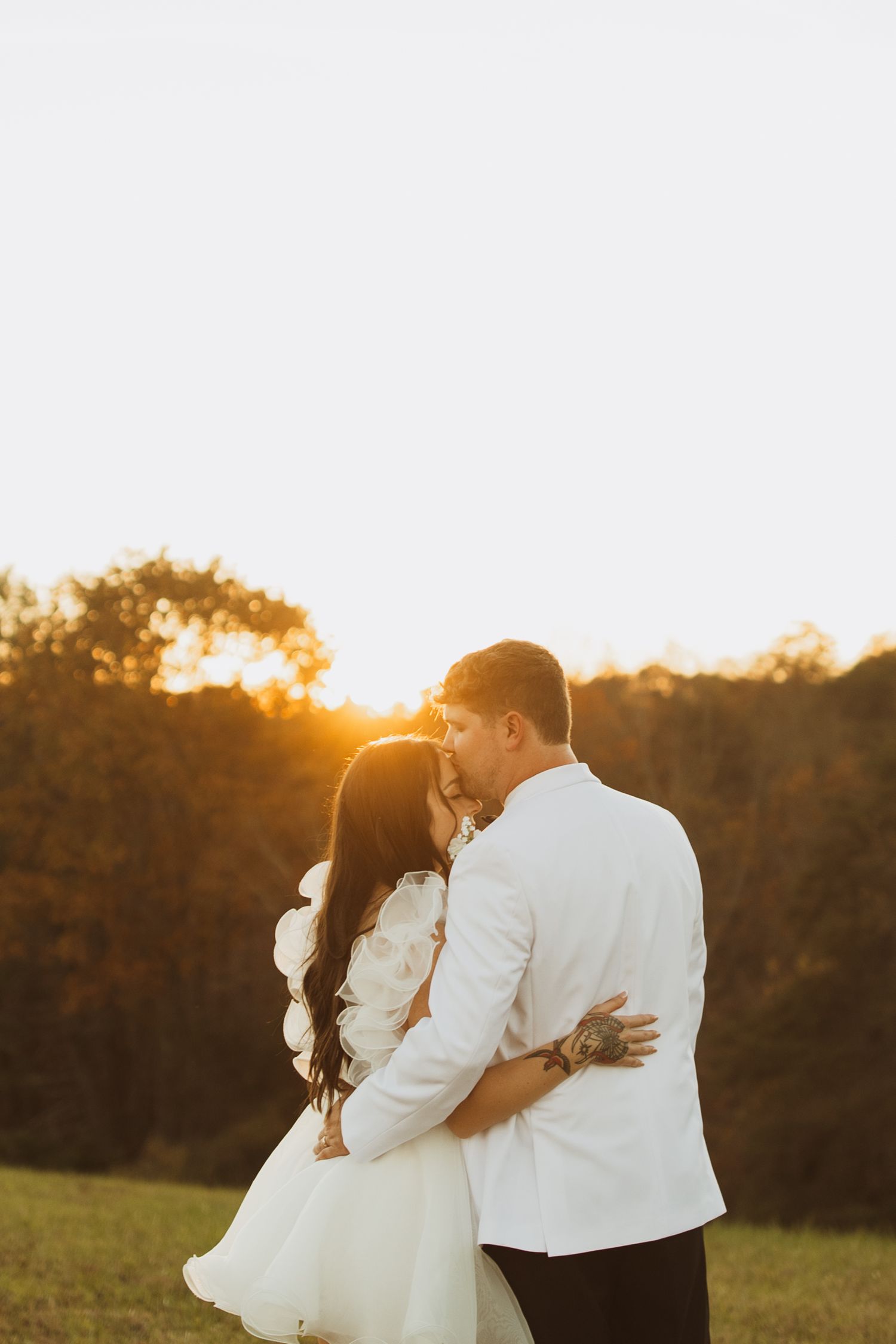 Romantic sunset embrace in white outfits during golden hour photoshoot.