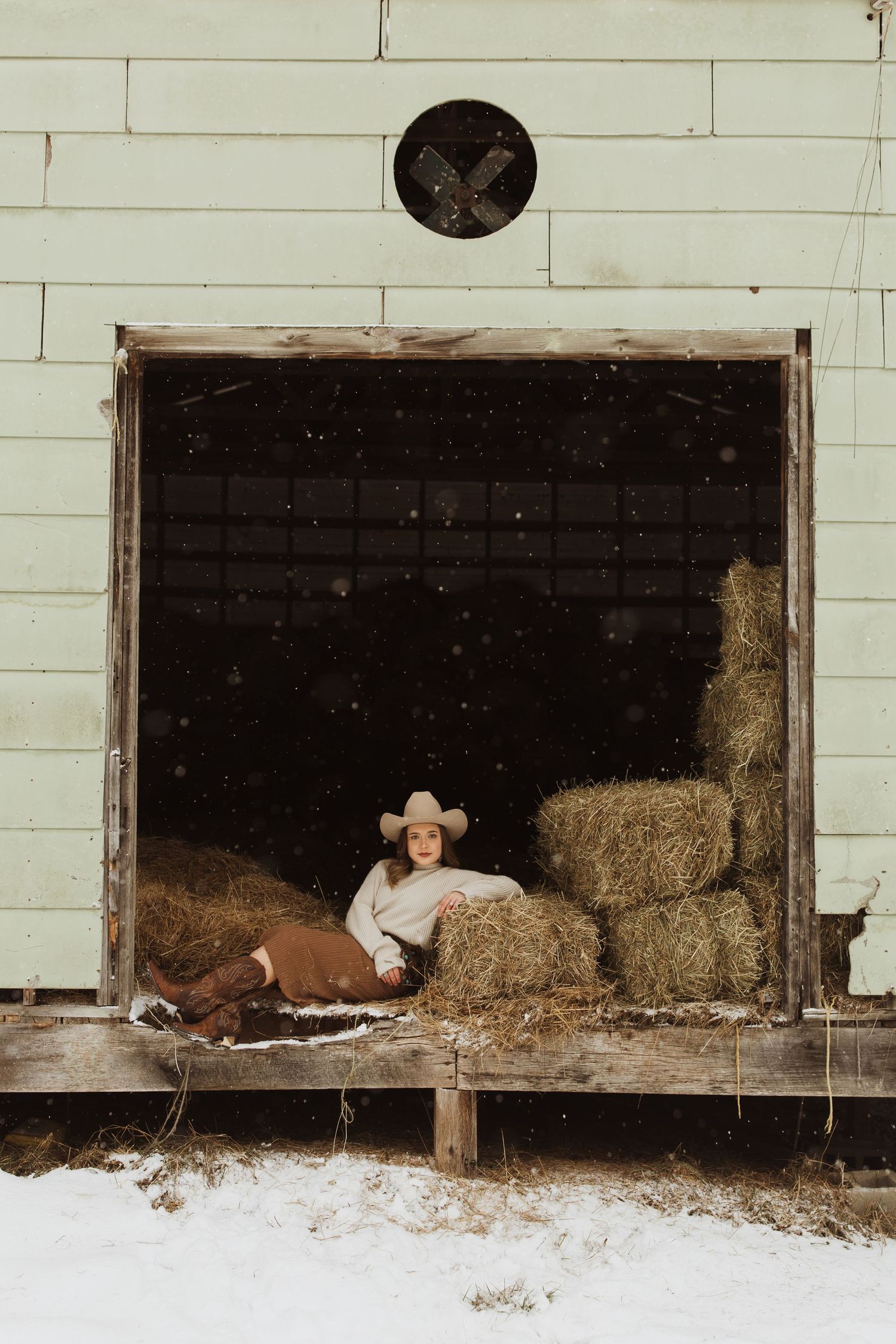 A winter barn scene with hay bales and white clapboard siding.