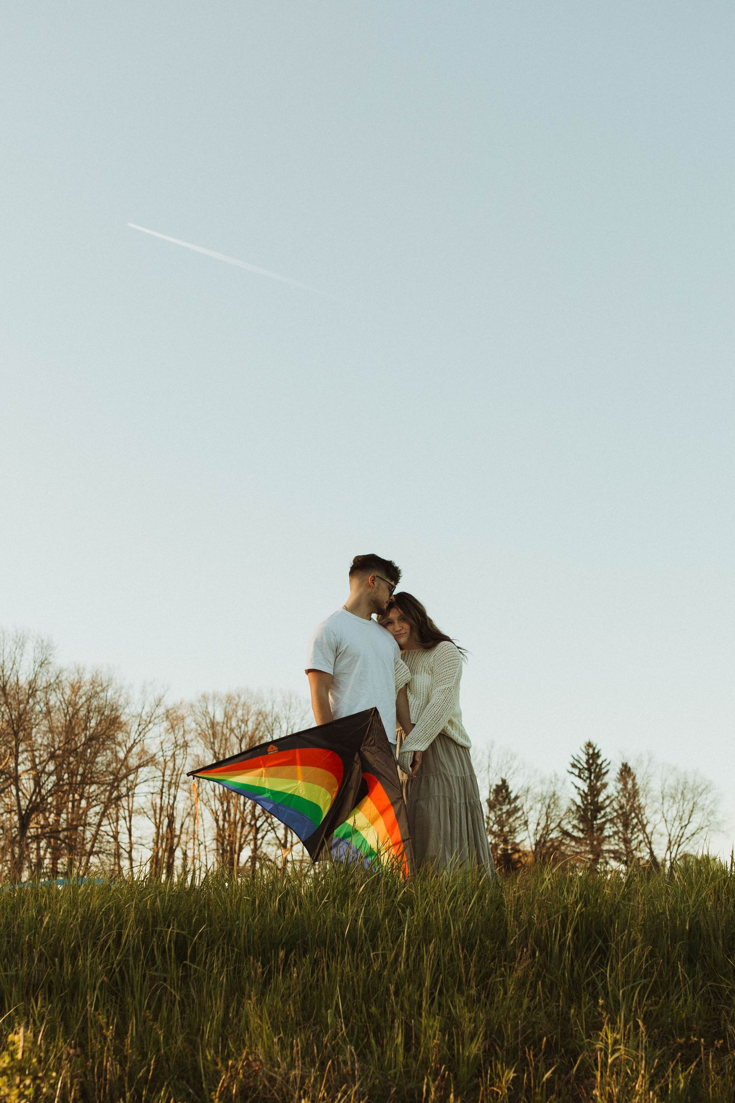 A couple shares an intimate moment on a hilltop with a rainbow kite at sunset.