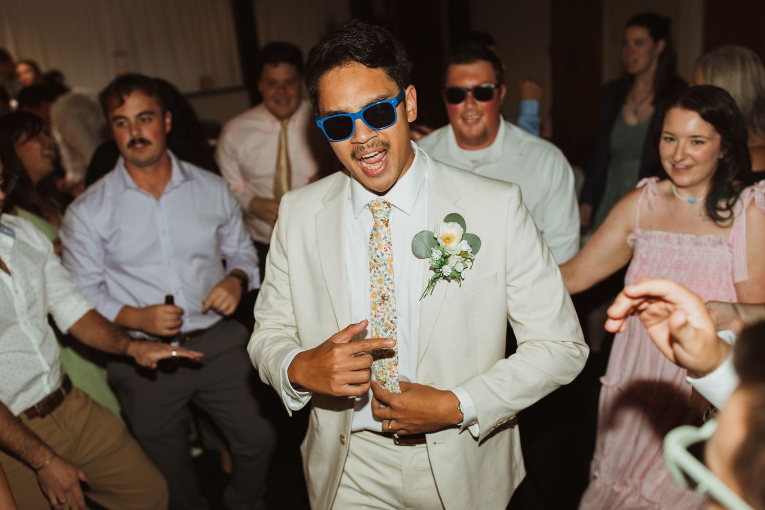 Wedding reception guests dancing and celebrating in formal attire and sunglasses.