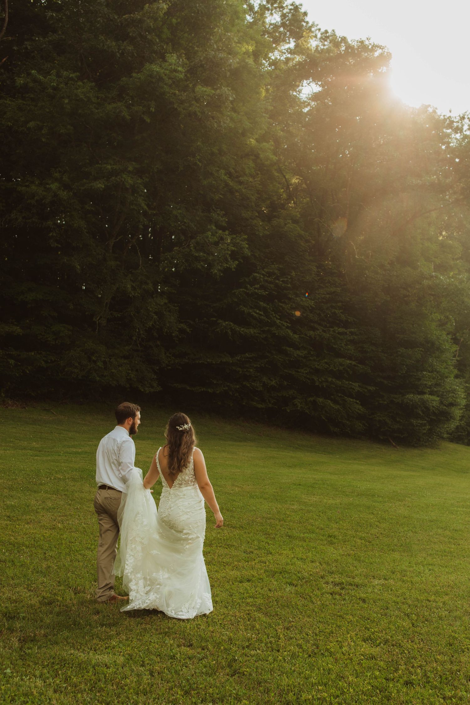 A couple walks hand in hand across a sunlit grassy hill.