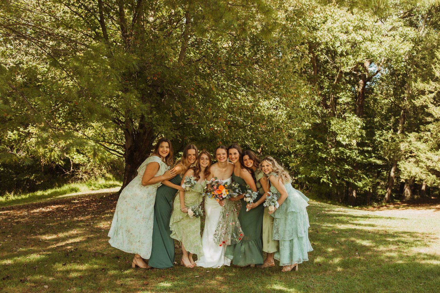 Wedding party in pastel blue dresses huddles together for a group photo in a sunny garden.