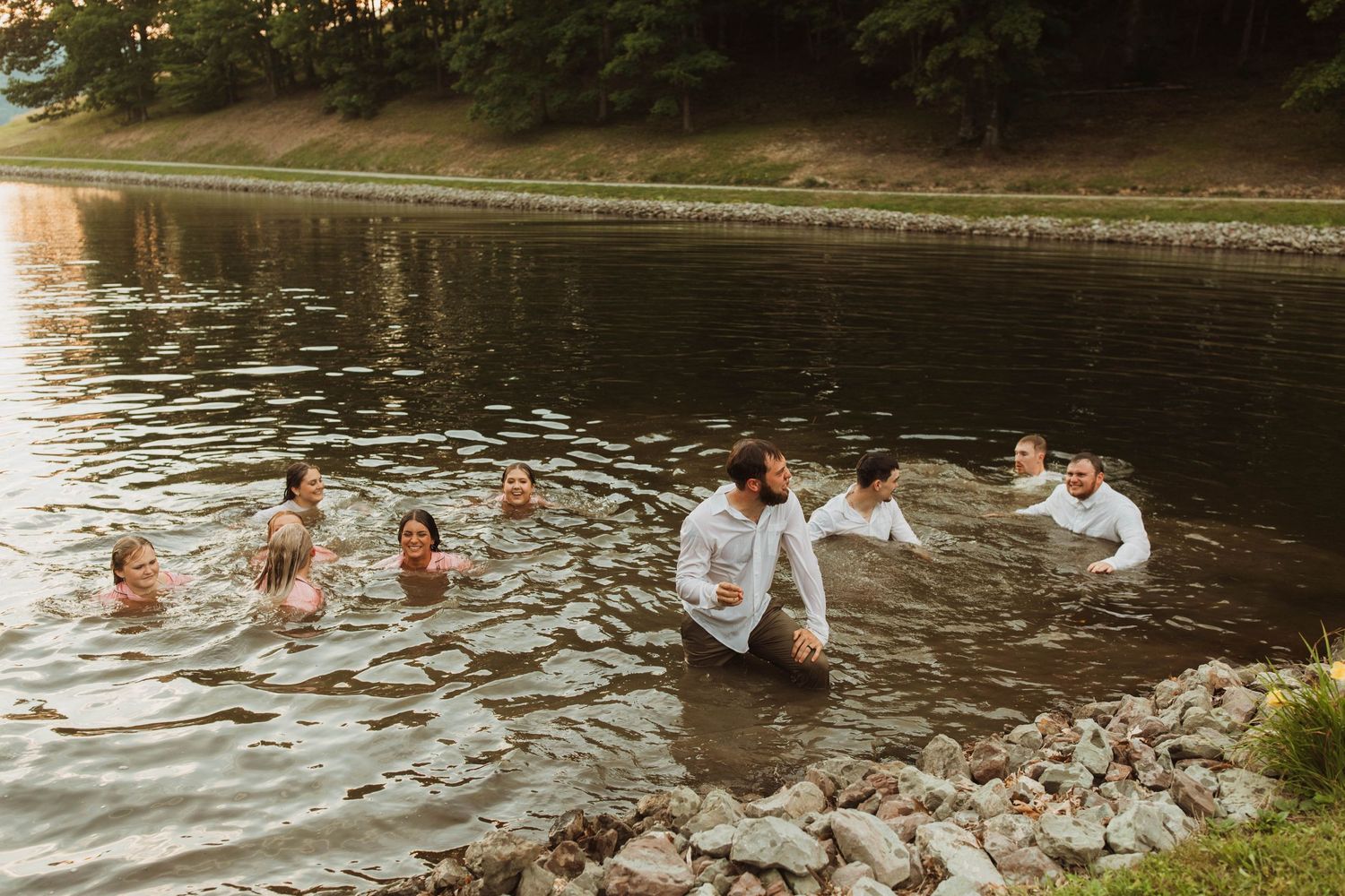 A group splashes and plays together in a scenic lake during a summer wedding celebration.