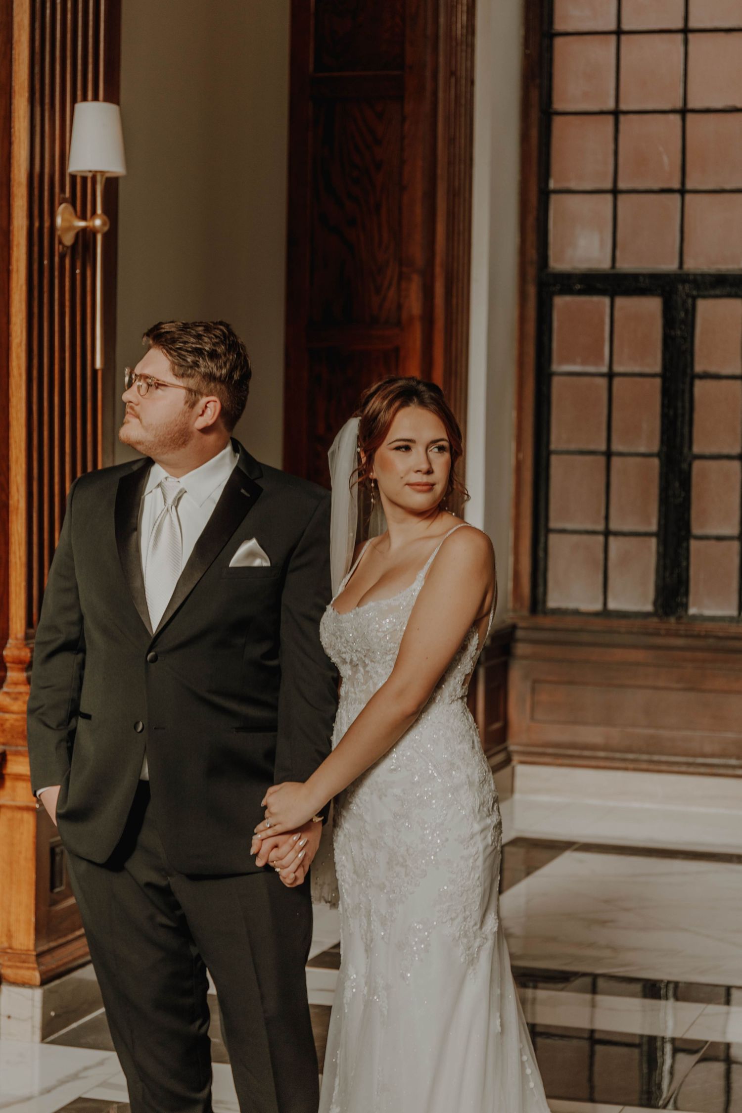 Newlyweds pose together in a historic building with wooden columns and ornate windows.
