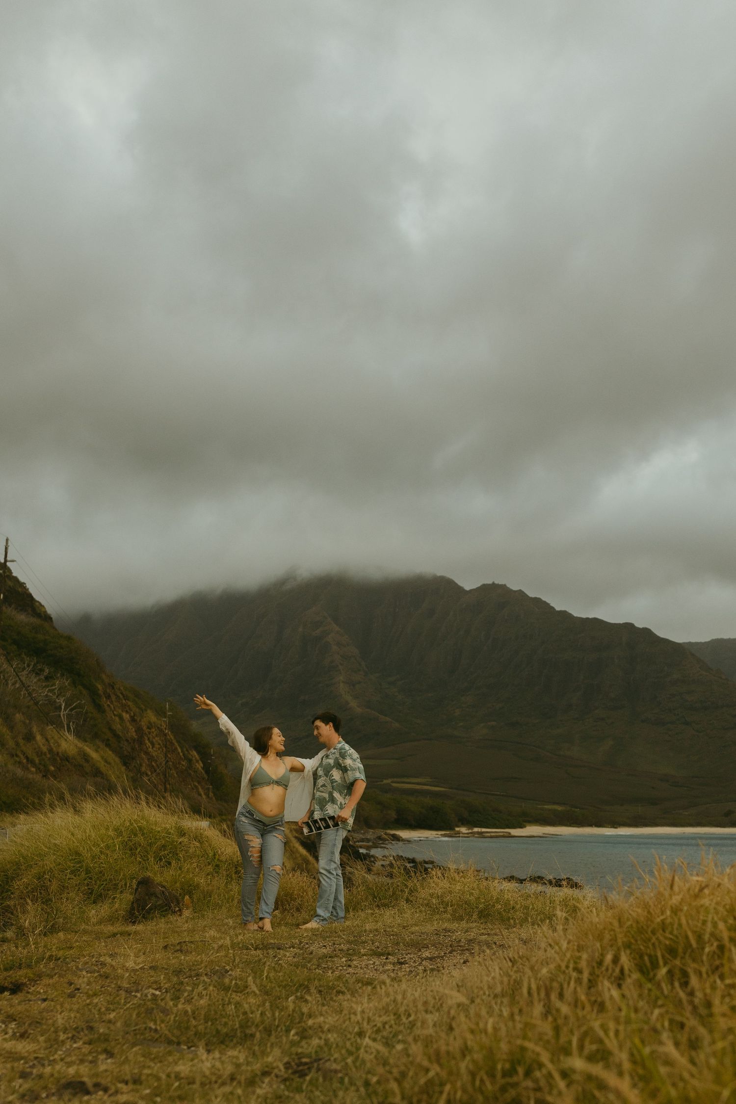 Couple enjoying a scenic moment on a hill overlooking a misty mountain lake in Hawaii.