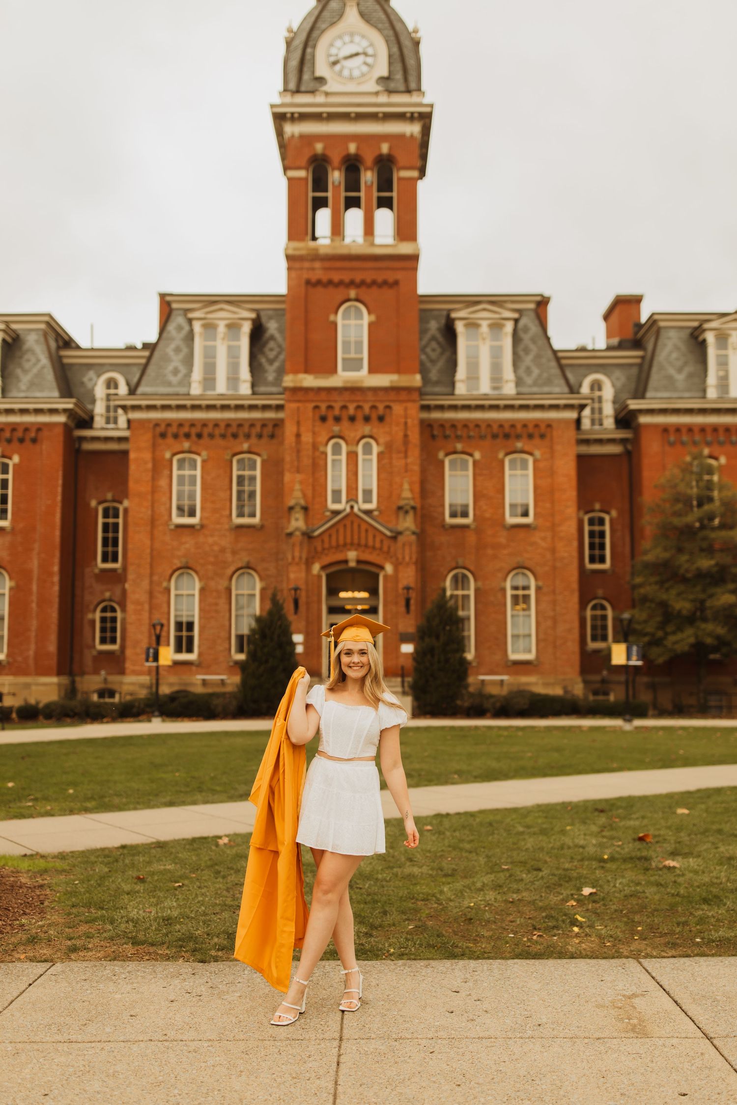 Figure in flowing orange cape and white dress walking in front of grand collegiate architecture.