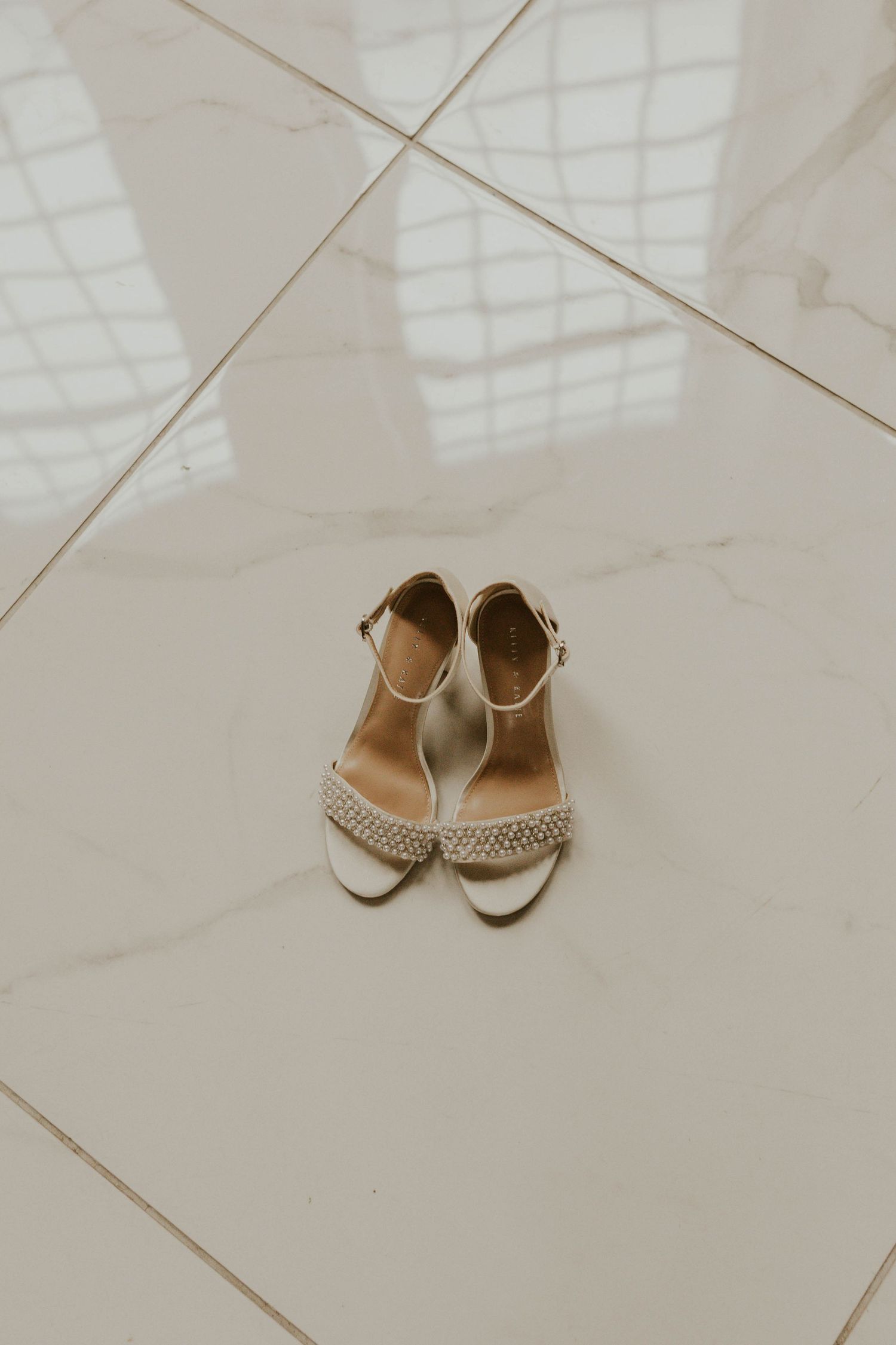 Elegant white bridal sandals with crystal details on light marble flooring.
