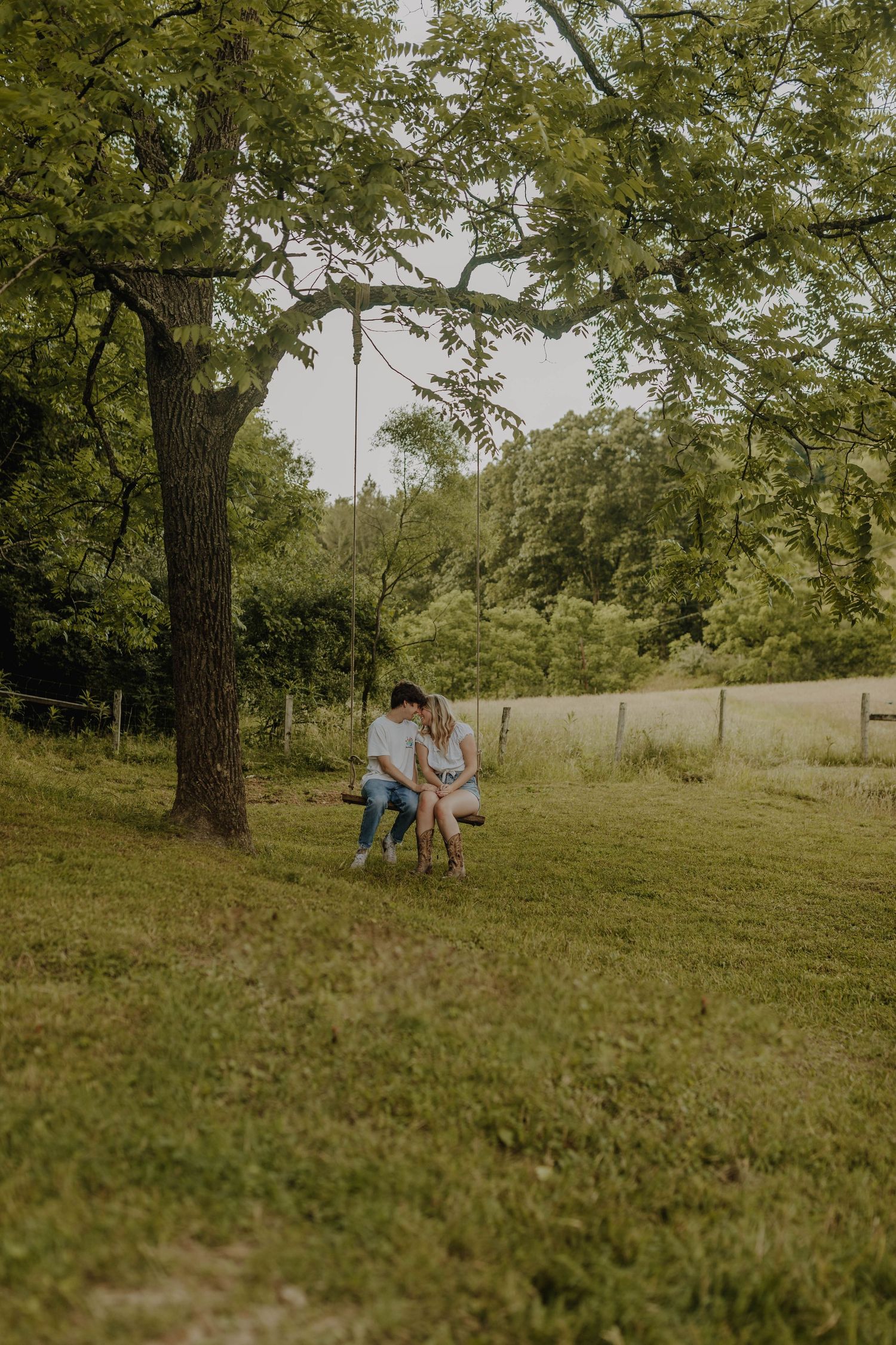 A couple sharing an intimate moment on a tree swing in a green summer meadow.