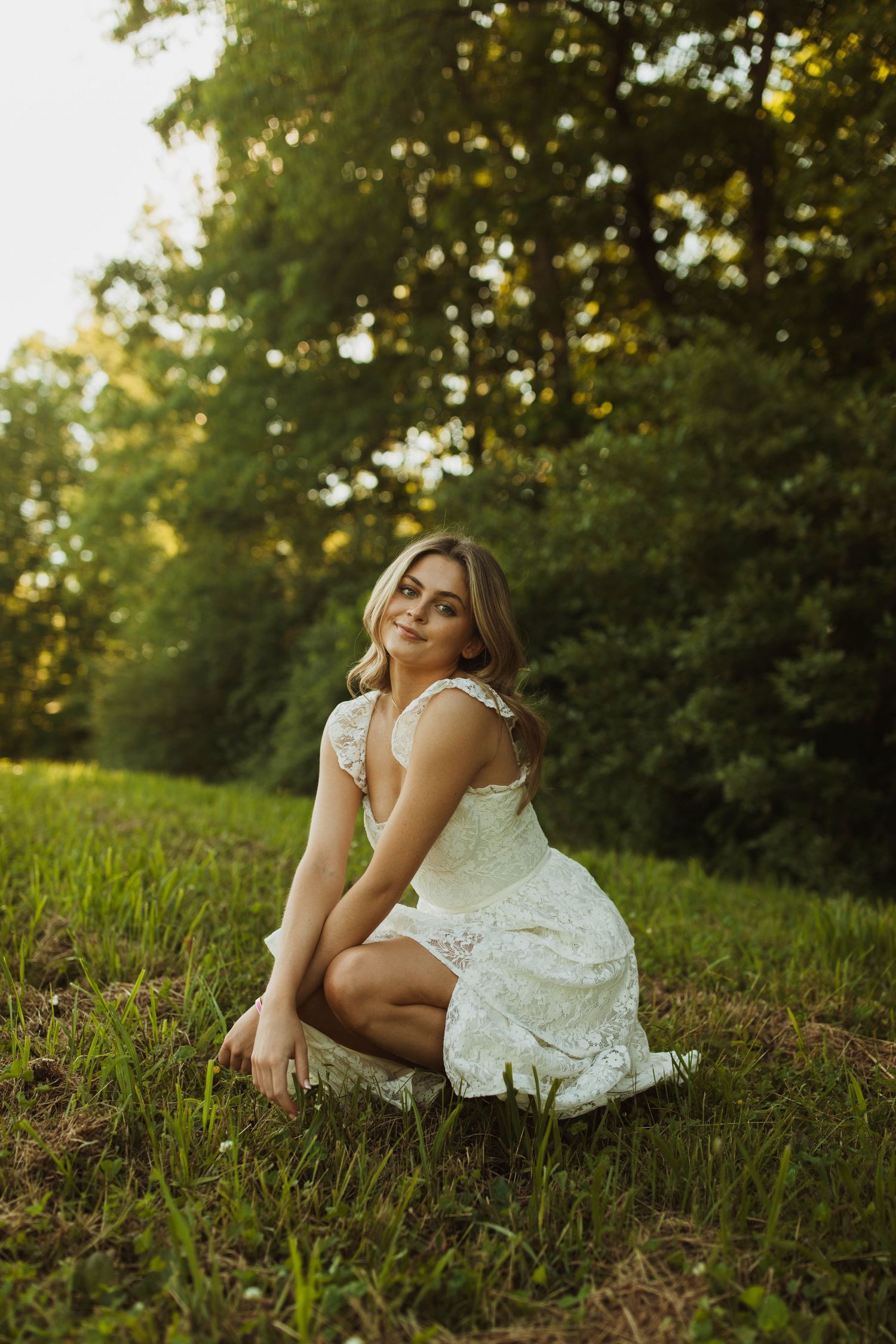 A white lace dress stands out against lush greenery in a golden hour portrait session.